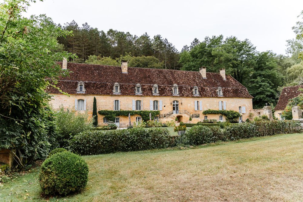 Historic stone manor house with climbing vines and traditional French architecture in a garden setting.