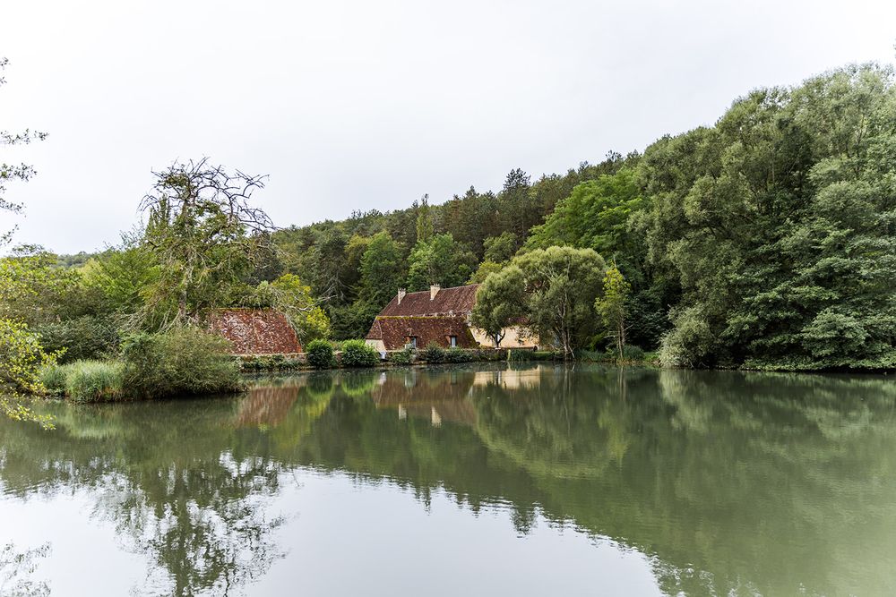 Tranquil countryside estate reflecting in a peaceful pond surrounded by lush greenery.