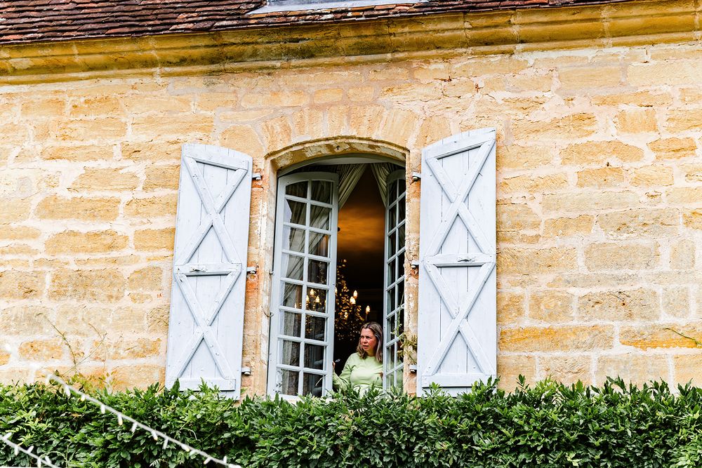 Rustic French window with white shutters and climbing plants on stone wall.