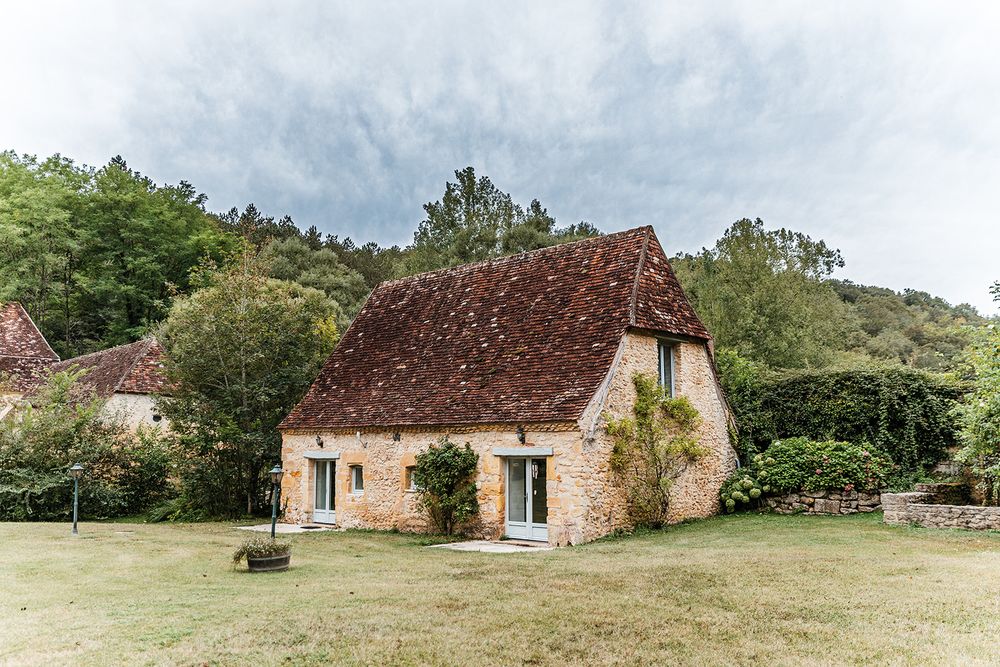 Quaint French country cottage with pink stone walls and rustic terracotta roof in a peaceful garden setting.