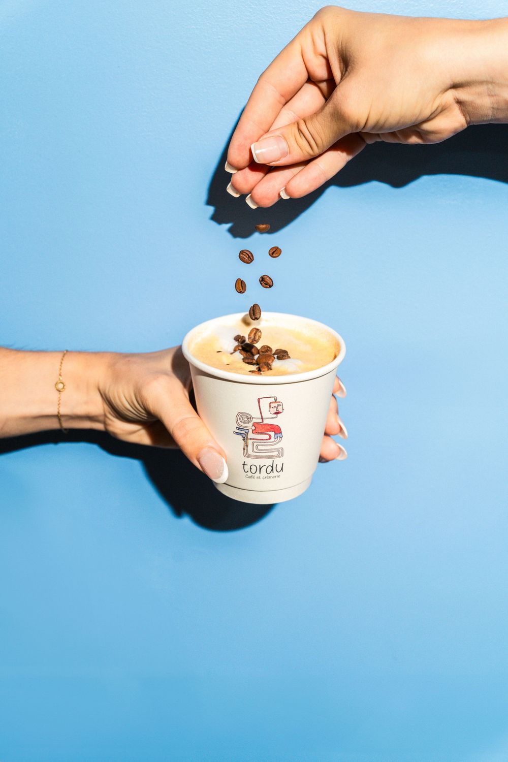 Hand sprinkling coffee toppings on a drink against blue background. Mtlshutter photography