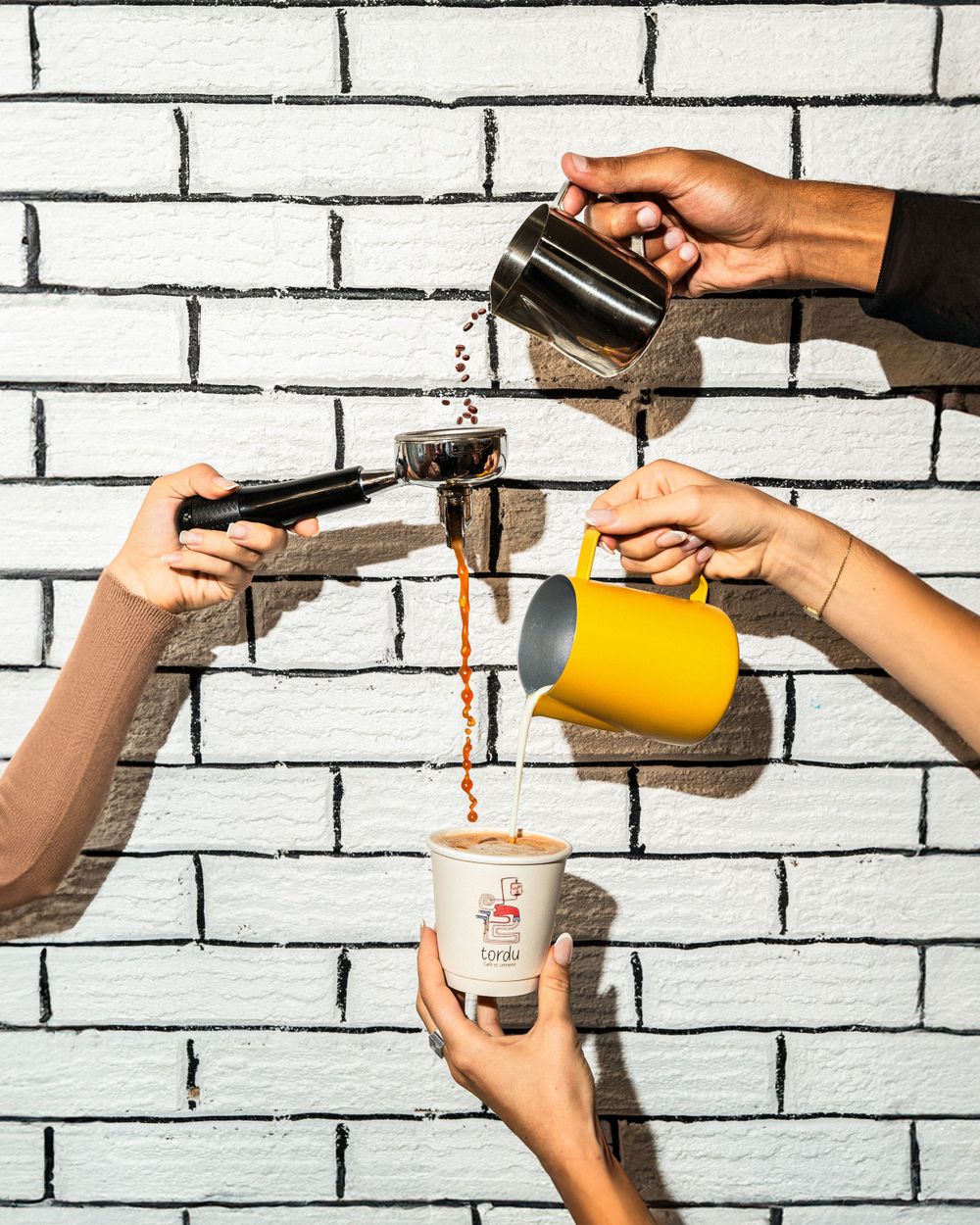 Multiple hands collaborating to pour and prepare coffee drinks against brick wall background. Mtlshutter photography