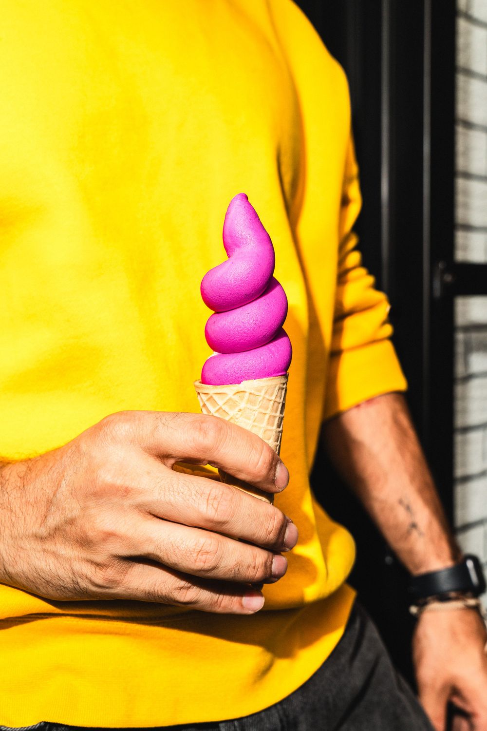 Bright pink soft serve ice cream cone held against yellow sweatshirt background. Mtlshutter photography
