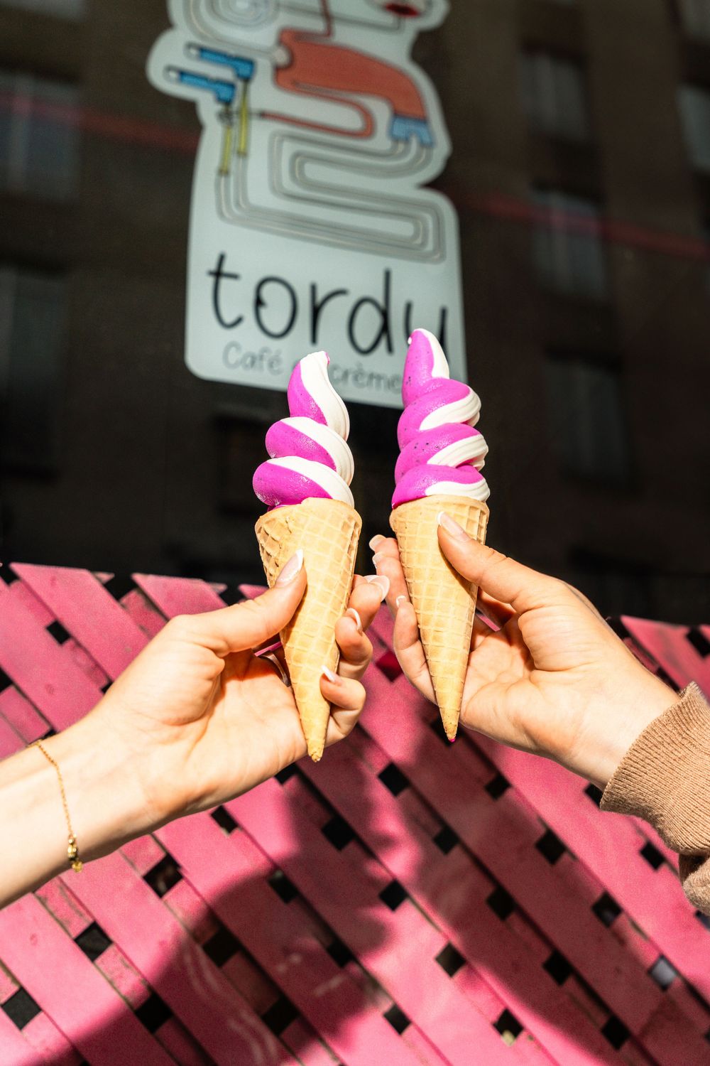 Two hands holding pink and white swirled ice cream cones under brand signage. Mtlshutter photography