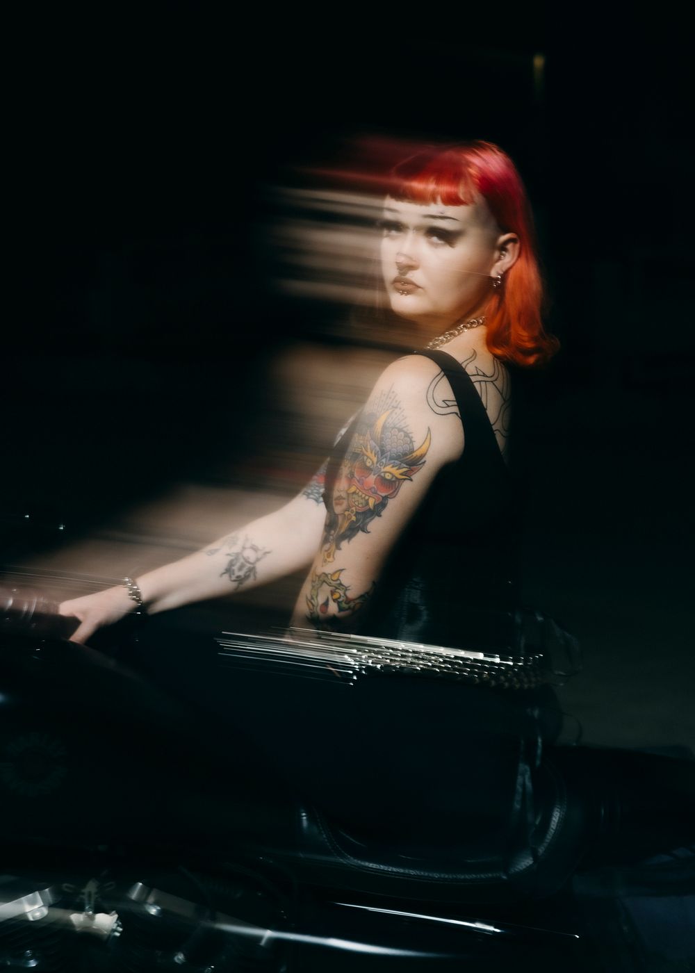 Model with tattoos and colourful hair on motorcycle at night, motion blur