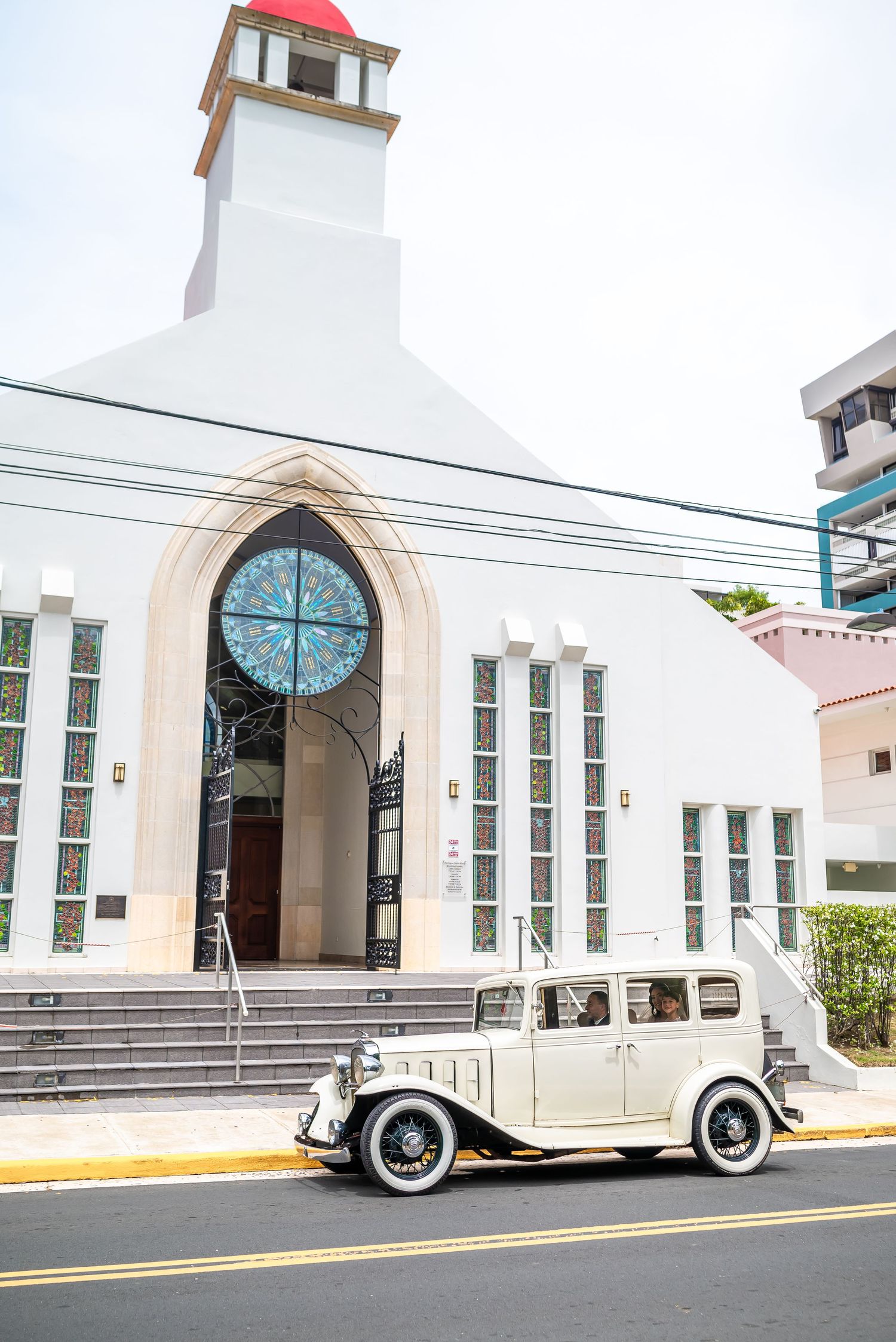 Classic white church exterior with vintage car parked in front on a sunny day.