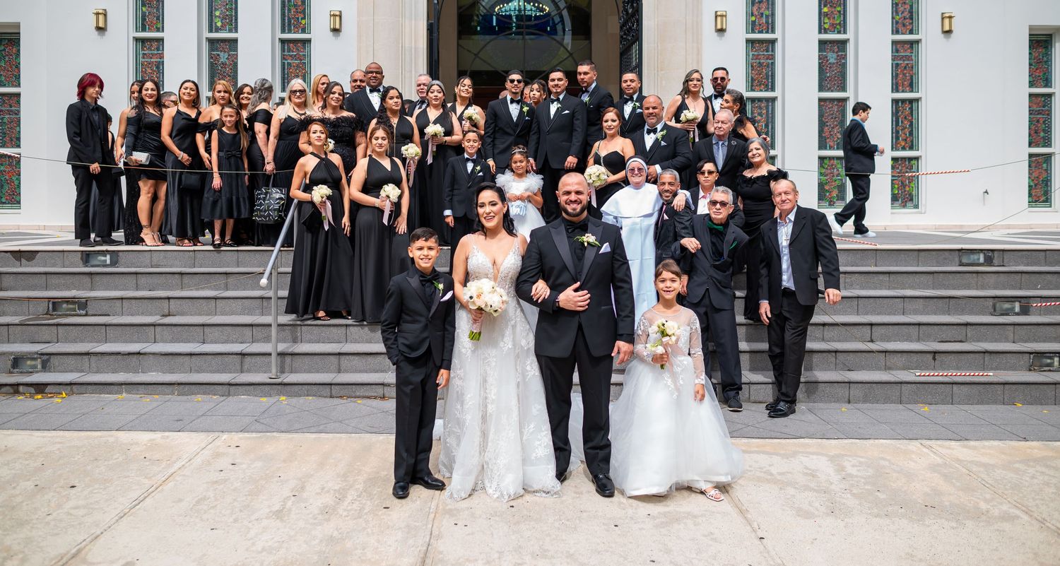 Large wedding party in formal attire posed on church steps.