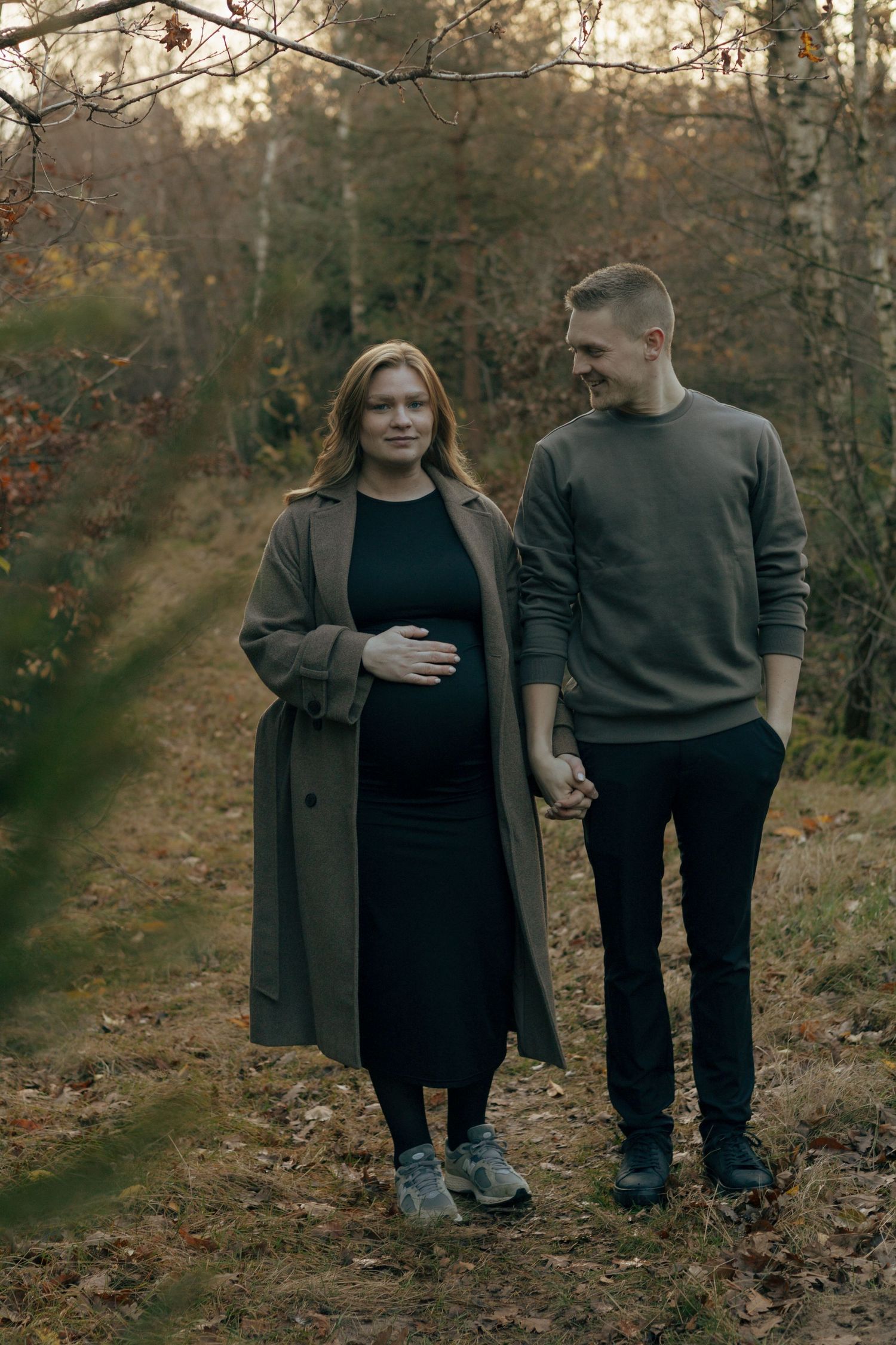 A couple walking hand in hand through an autumn forest path.