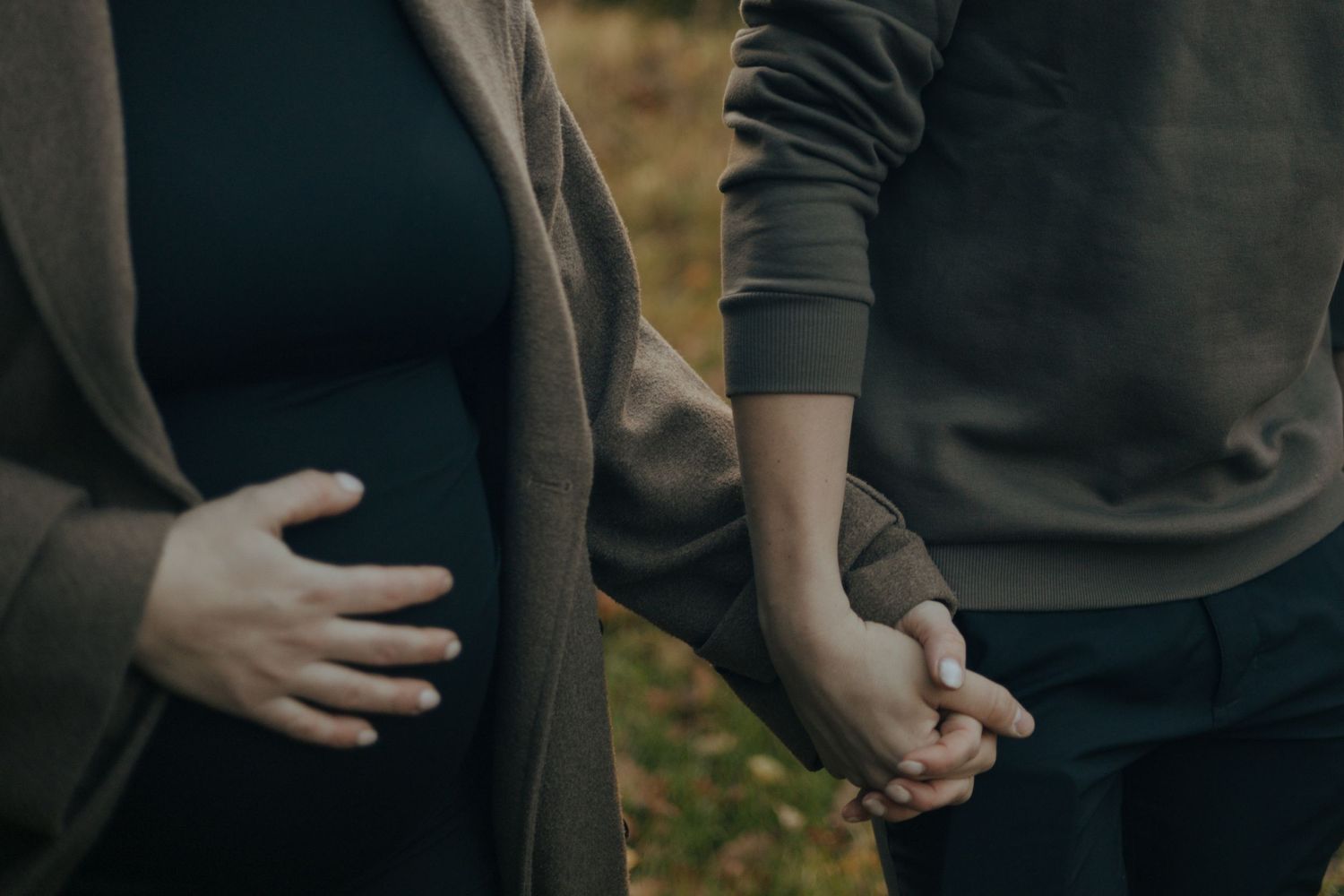 Close-up of joined hands against autumn foliage background.