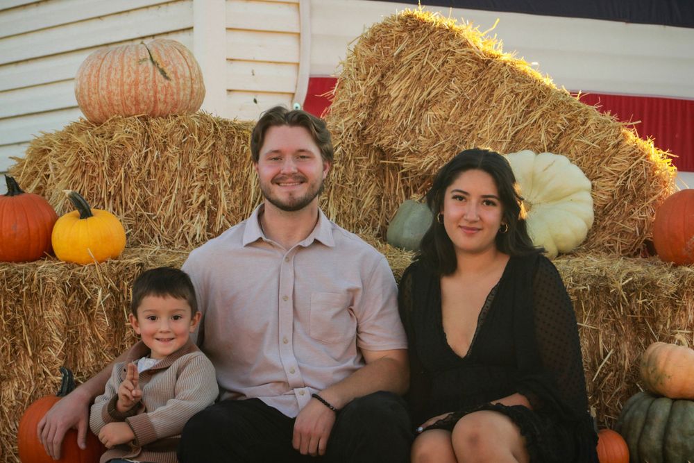 Family poses together on hay bales with pumpkins at a rustic fall photo shoot.