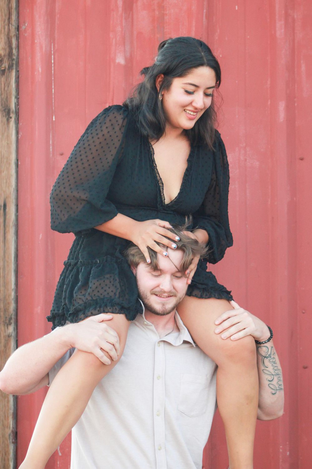 Couple shares lighthearted moment with shoulder ride against red backdrop.