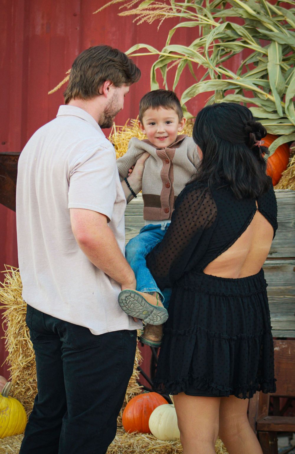 Family interacts with child near rustic fall display with hay and pumpkins.