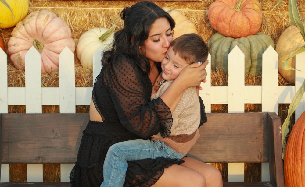 Mother and child share tender moment on bench with autumn decorations.