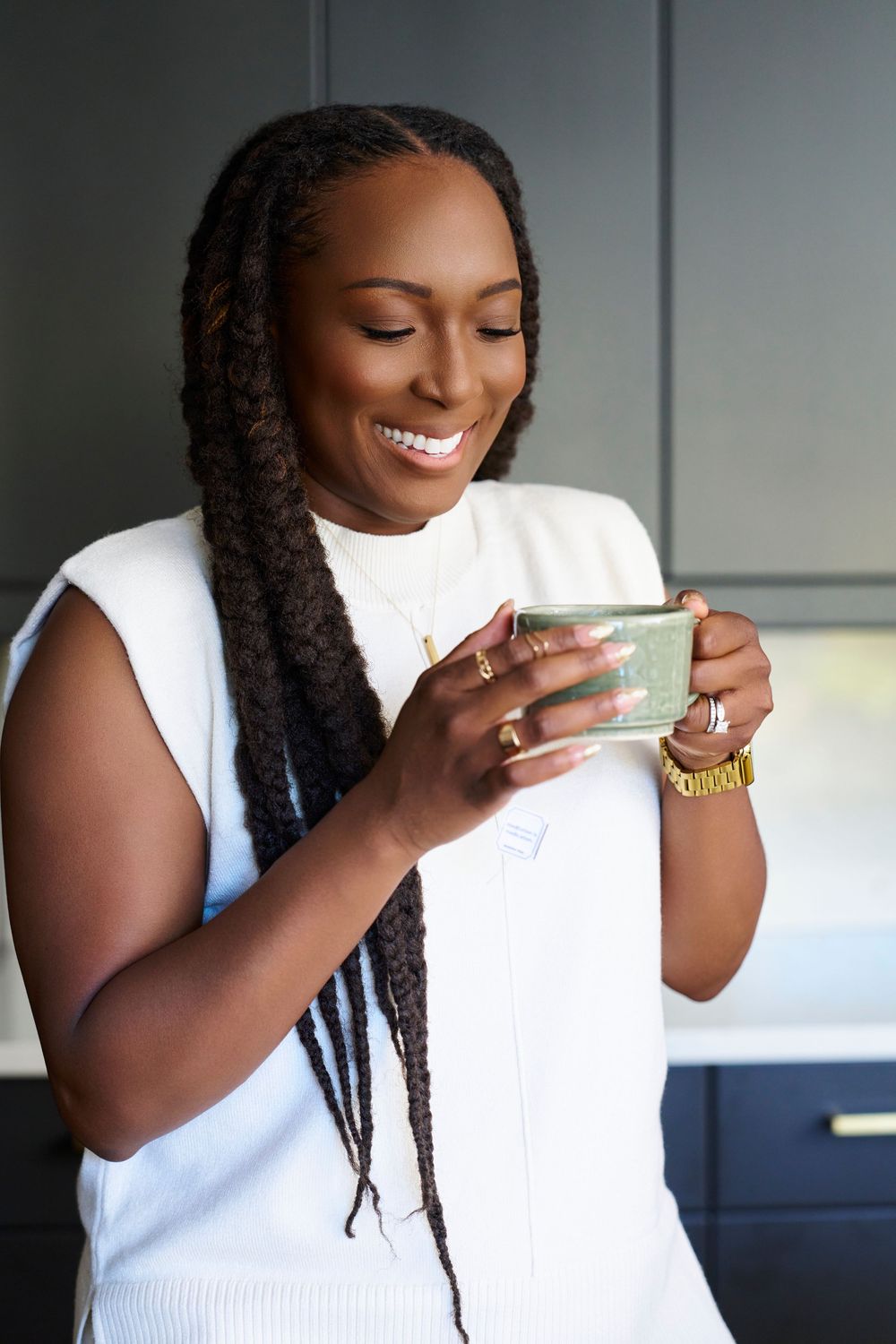 Person enjoying coffee with a bright smile while wearing a white sleeveless top.