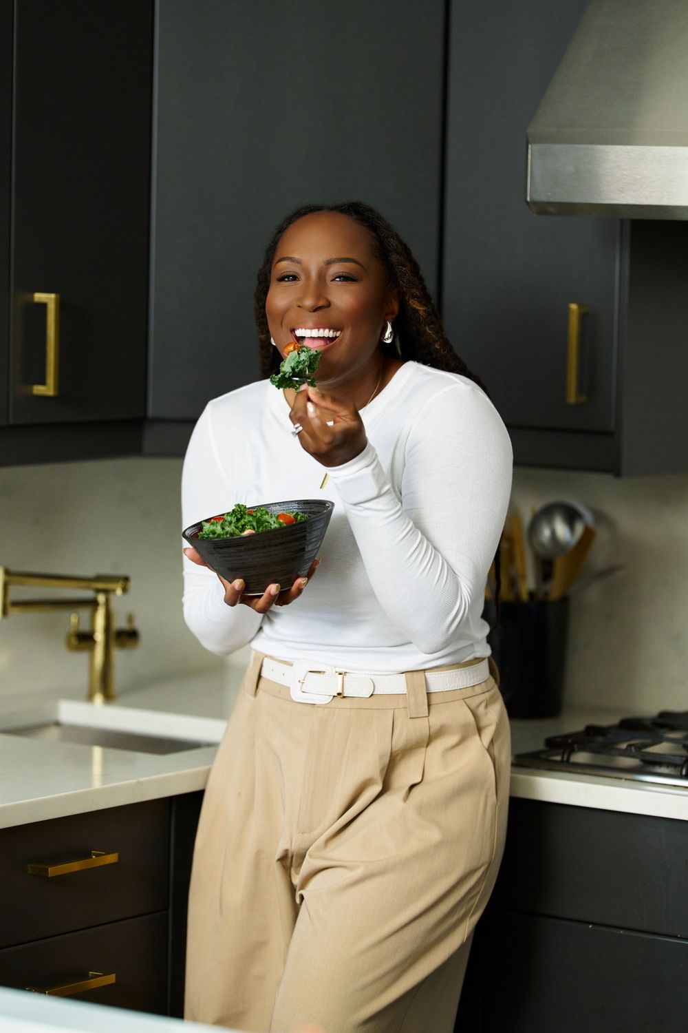 Person enjoying healthy food in stylish kitchen with dark cabinets and gold accents.