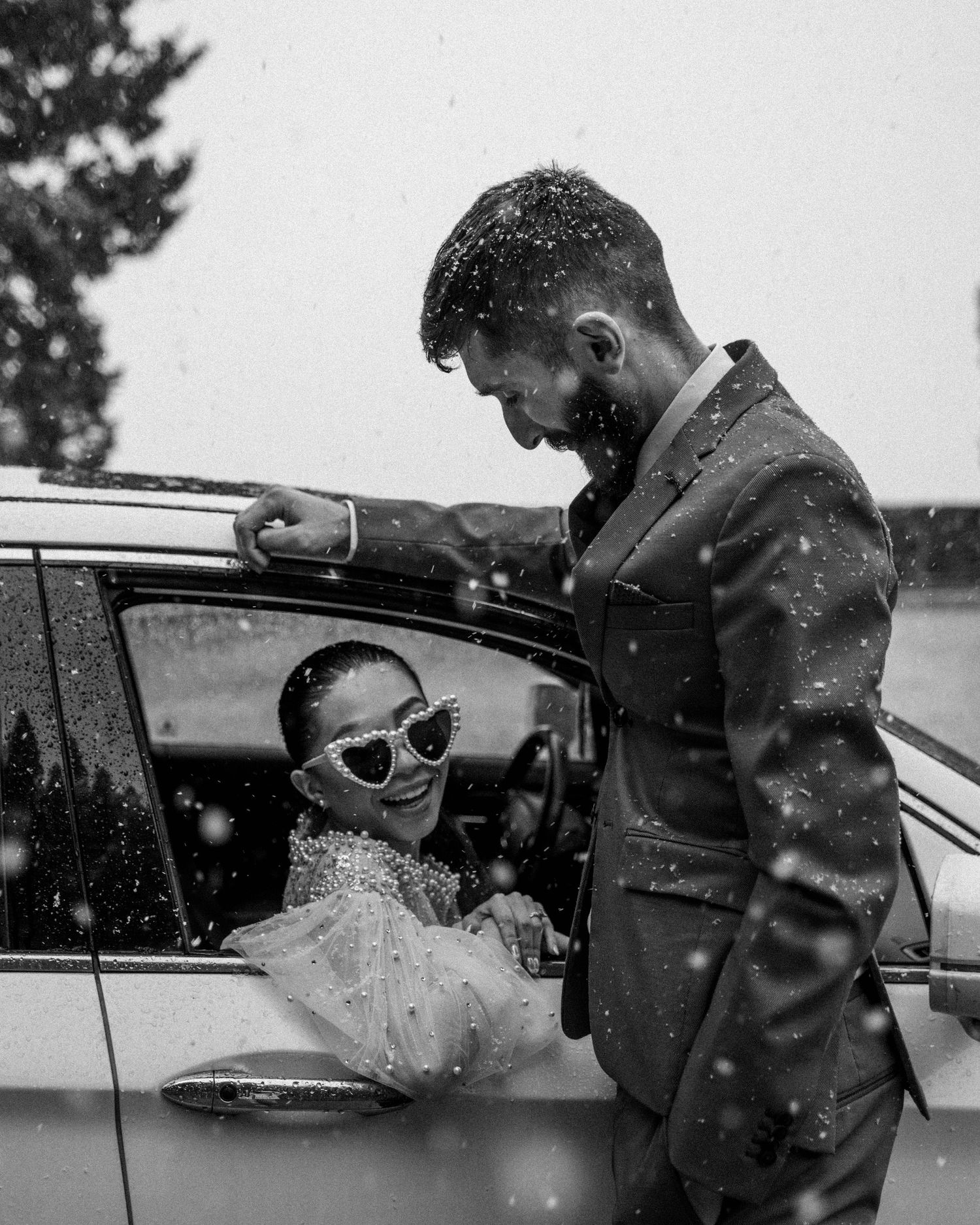 Bride sits in a car in the snow.