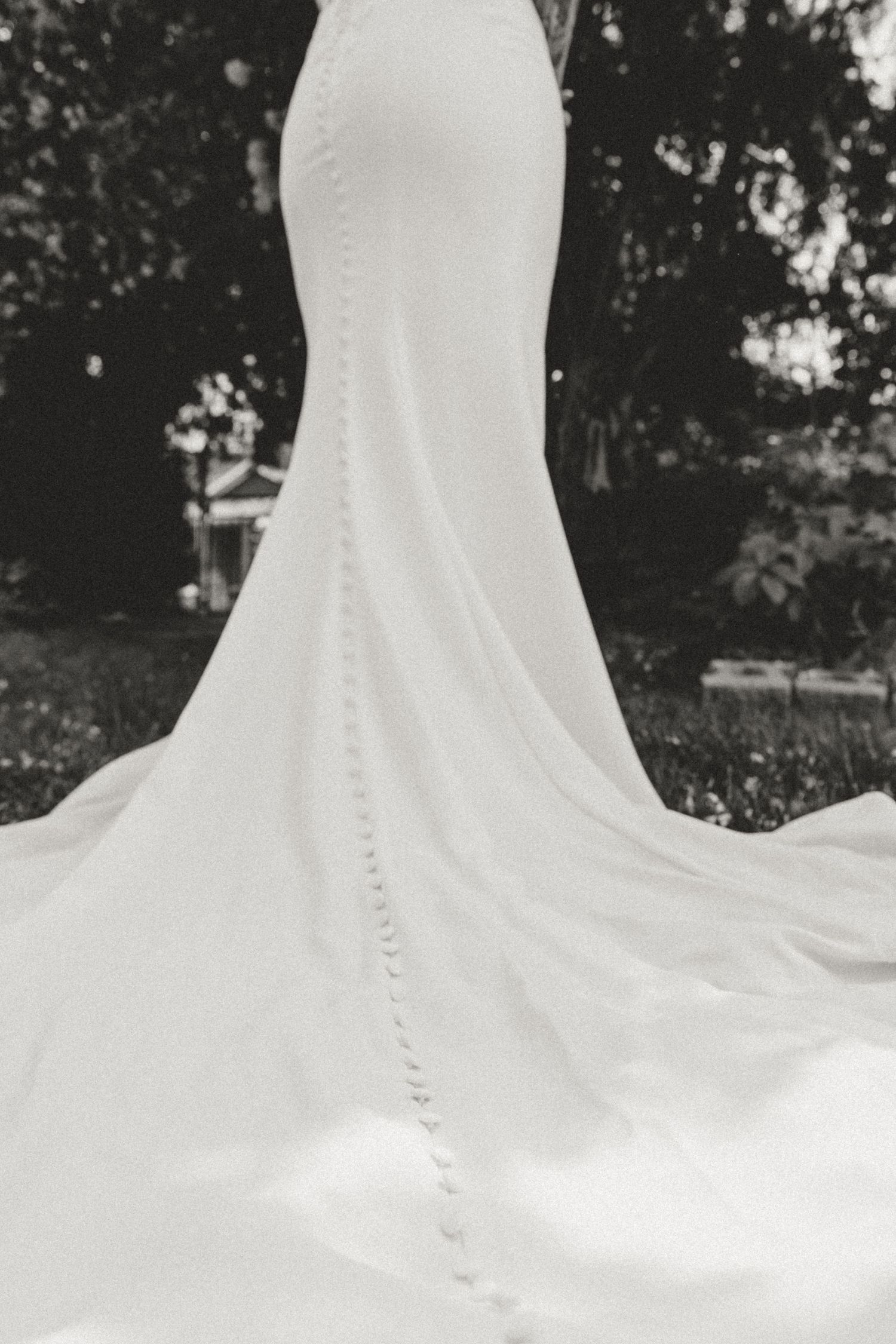 Elegant mermaid wedding dress with button details flowing on grass in black and white.