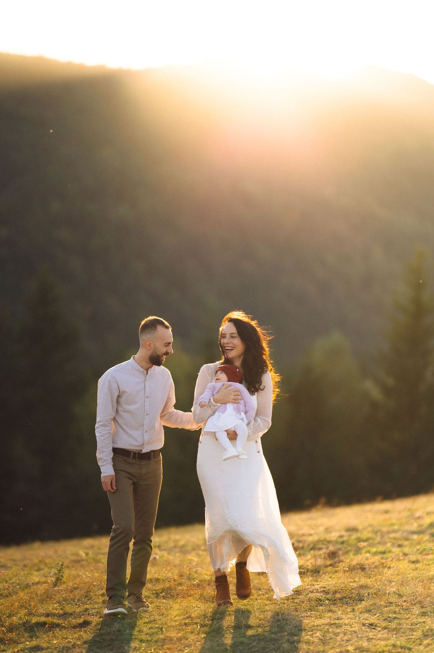 A couple walks together on a grassy hillside during golden hour.