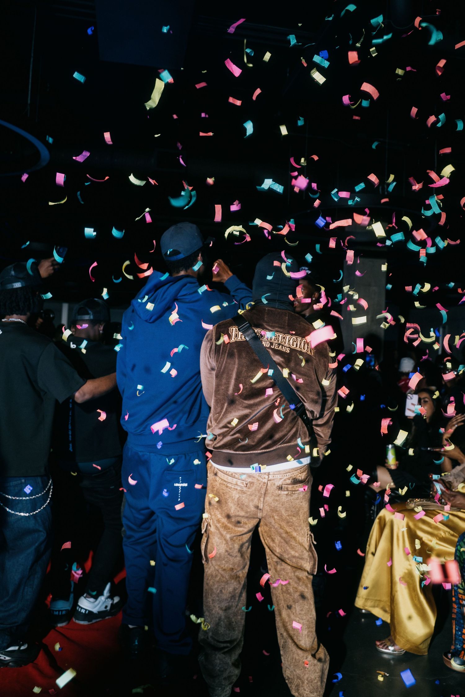 People celebrating under colorful confetti at a dark nightclub party event.