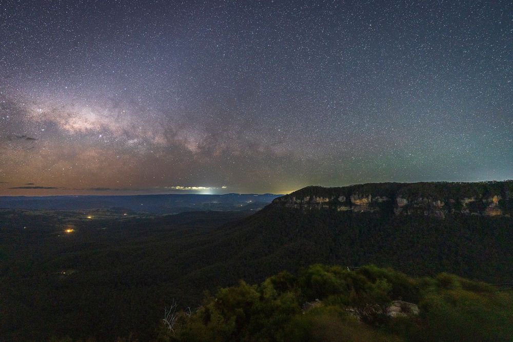 Milky Way galaxy arching over a dramatic mountain valley landscape under a stunning starry night sky.