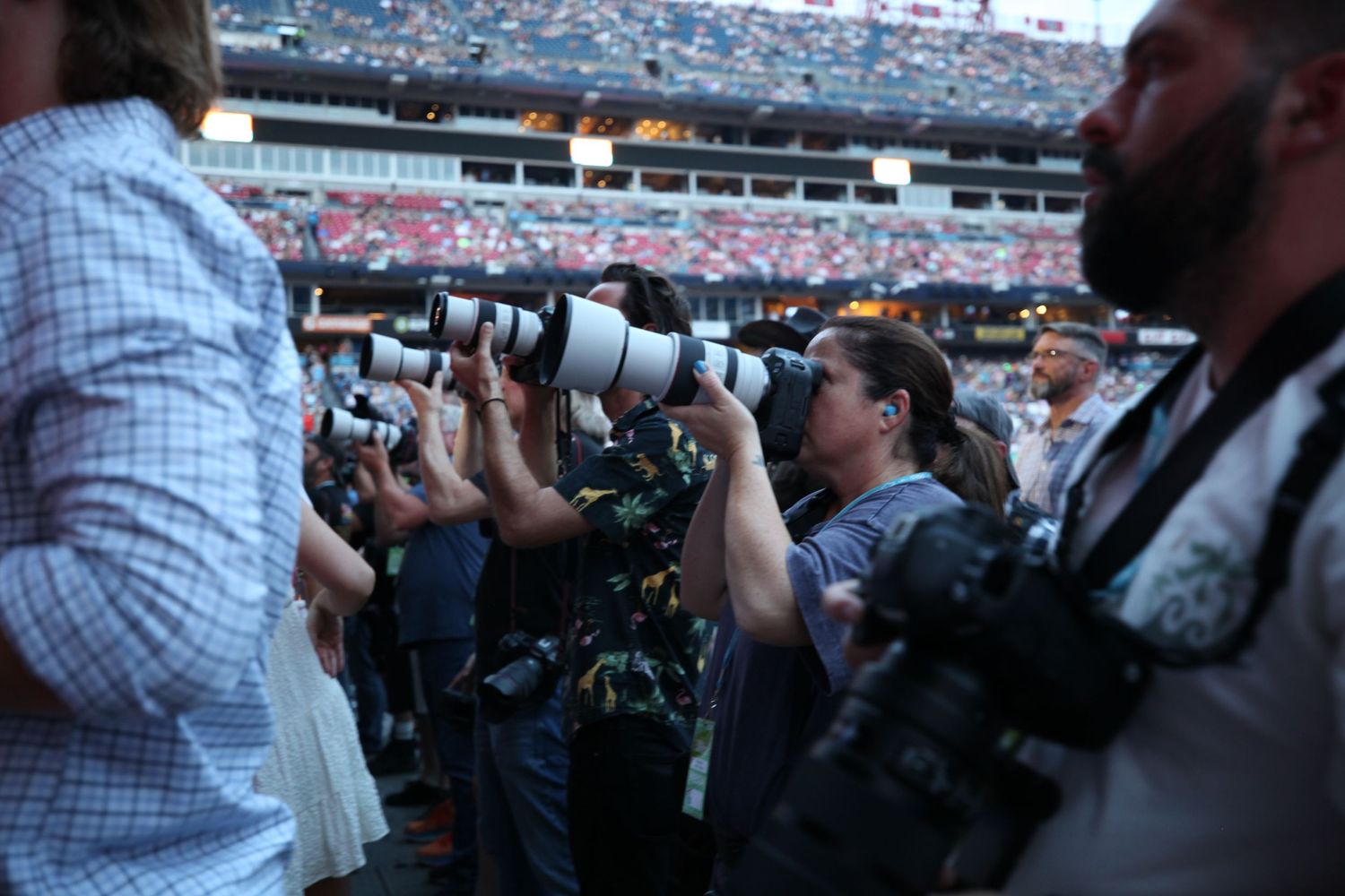 Row of professional photographers with cameras at crowded stadium event.