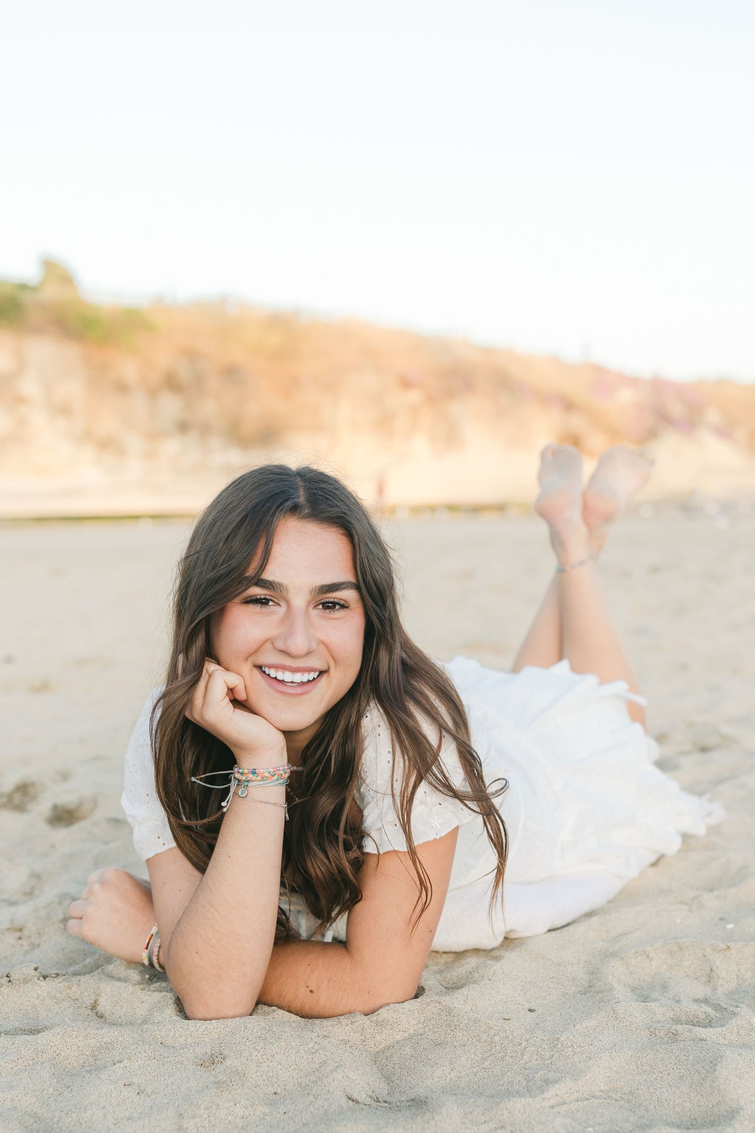 Graduating senior in white dress lying on beach during golden hour photography session with Senior photos with Chelsee Rawe Photography