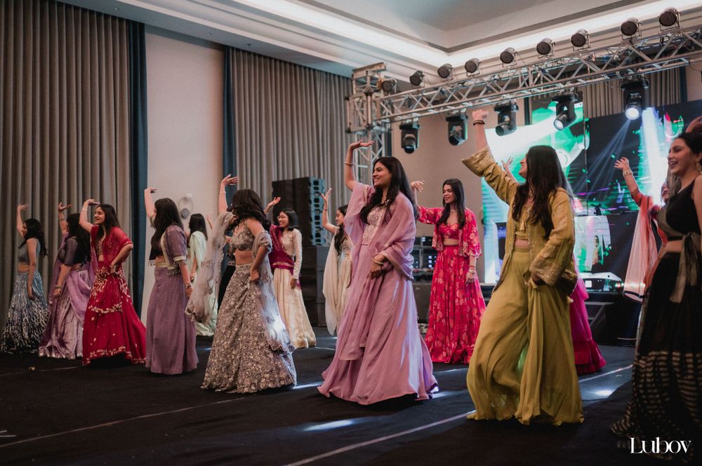 Wedding guests in colorful formal attire dance on a stage with theatrical lighting.