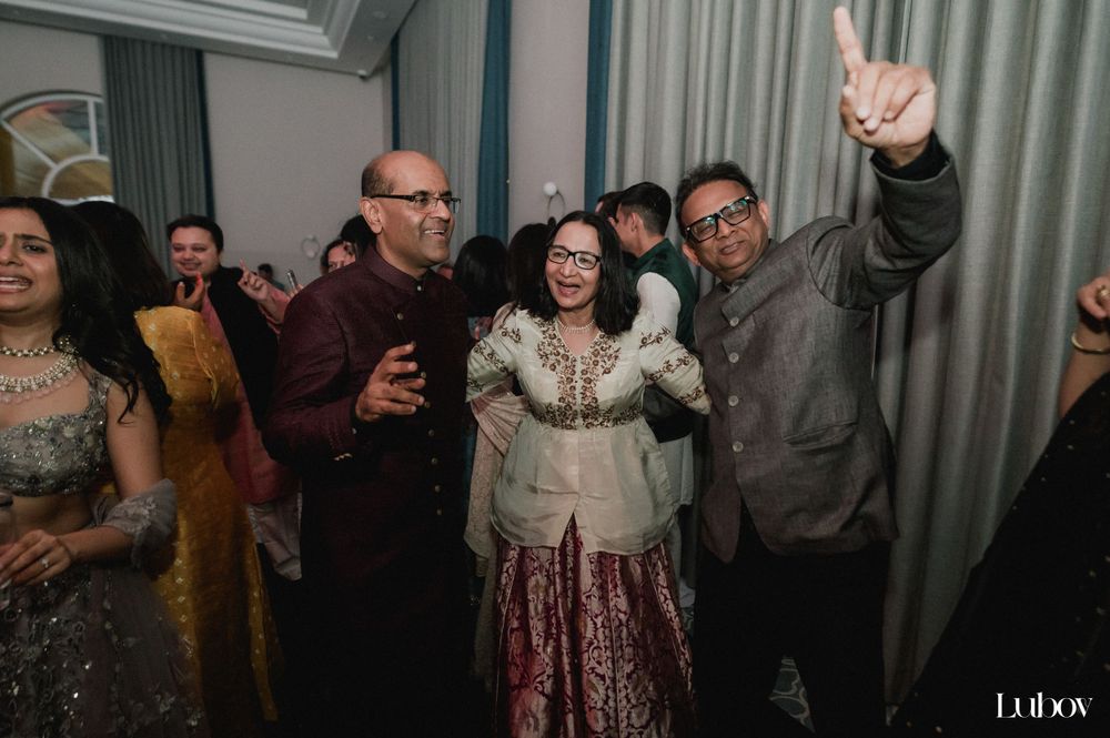 Wedding guests celebrate enthusiastically at an indoor reception with dramatic lighting.