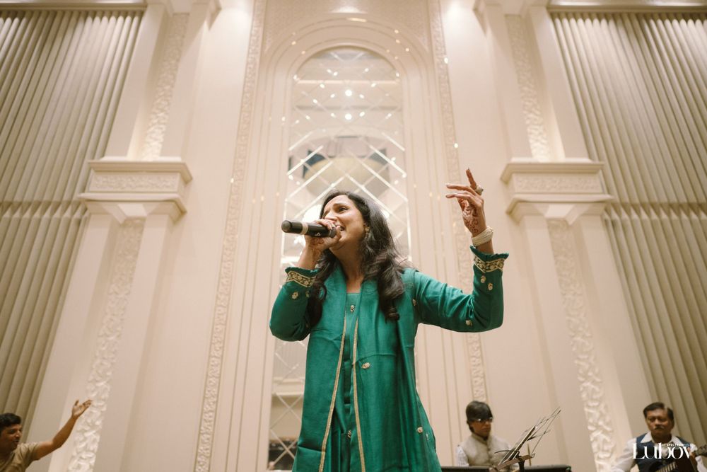 A performer in a green dress sings passionately on stage with dramatic lighting.