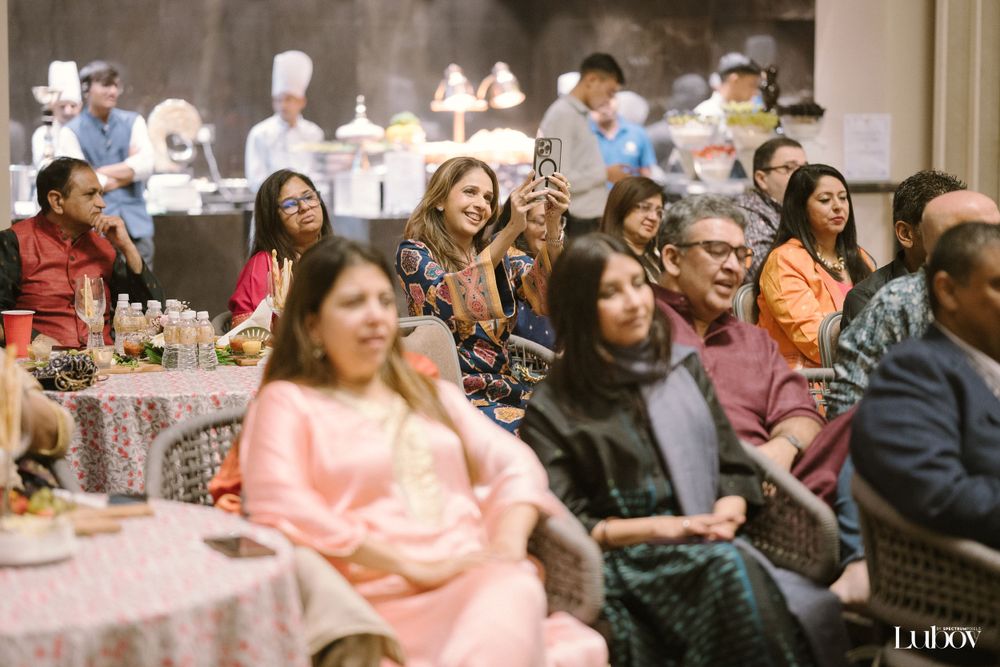 Audience members seated at decorated tables enjoy an indoor event.