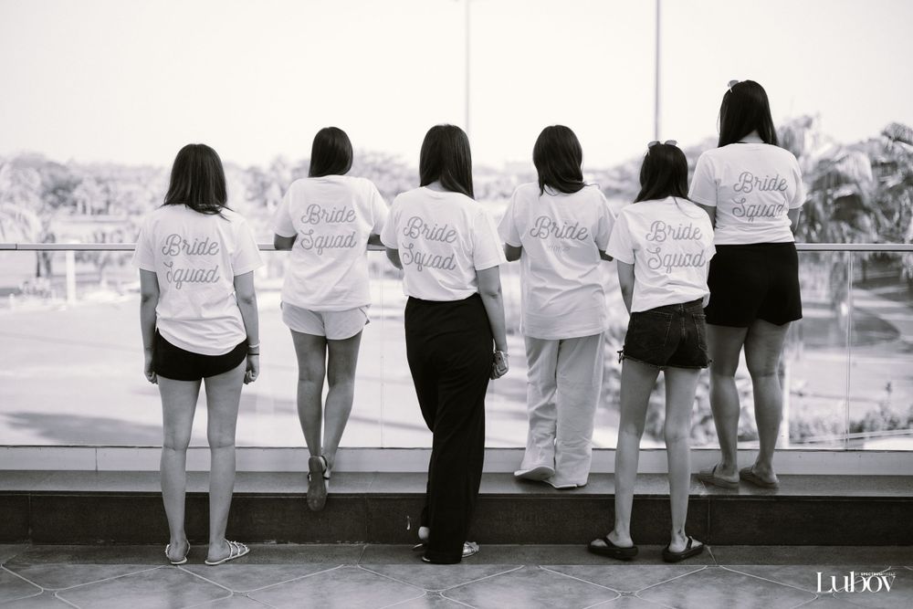 Group in white shirts stands at balcony railing in black and white photography.