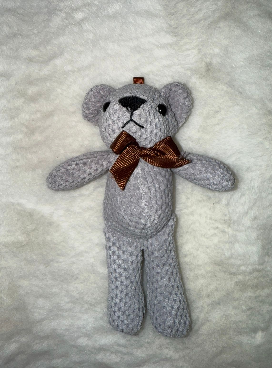 Gray knitted teddy bear with brown ribbon bow on white background.