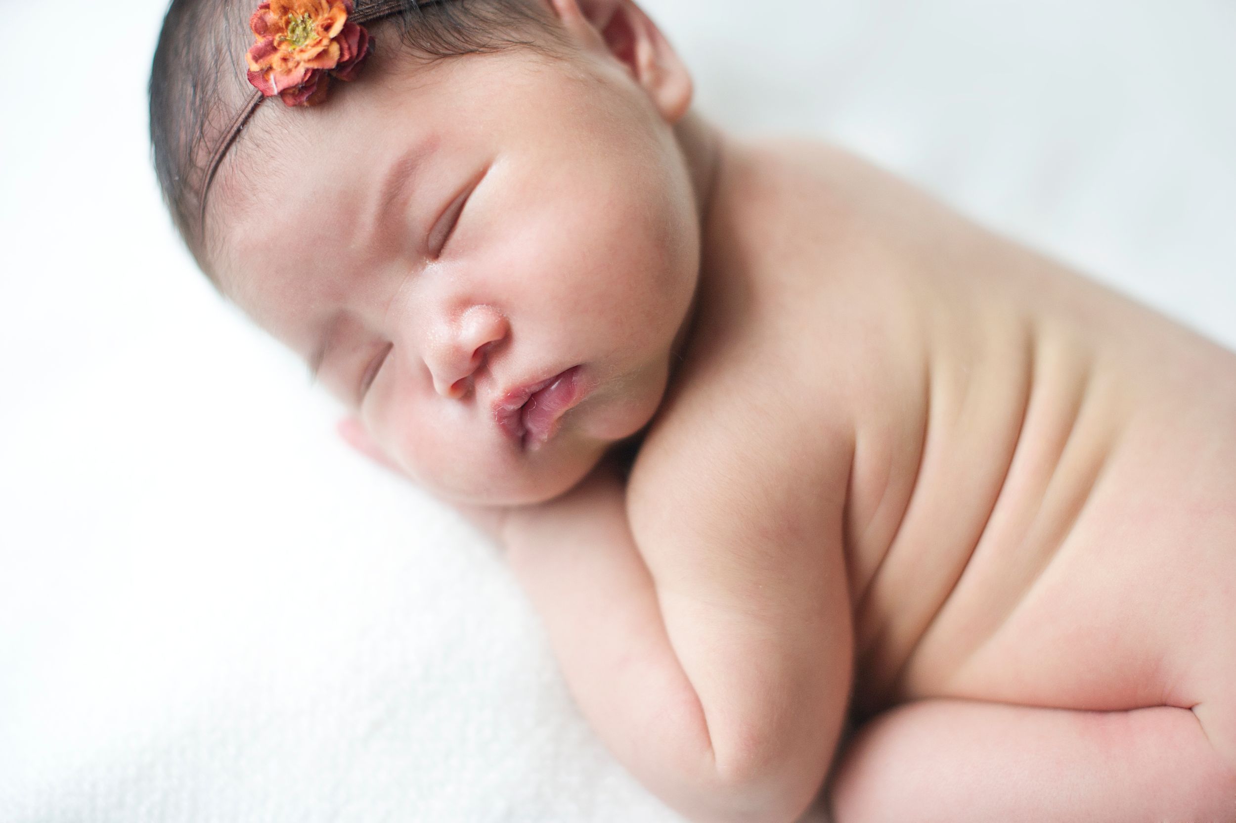 Sleeping newborn girl with a small flower headband showing sweet back rolls, photographed by Phoebe Lee Photo in Toronto
