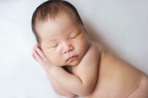 Sleeping newborn posed with hands on chest on a white blanket, photographed by Phoebe Lee Photo in Toronto