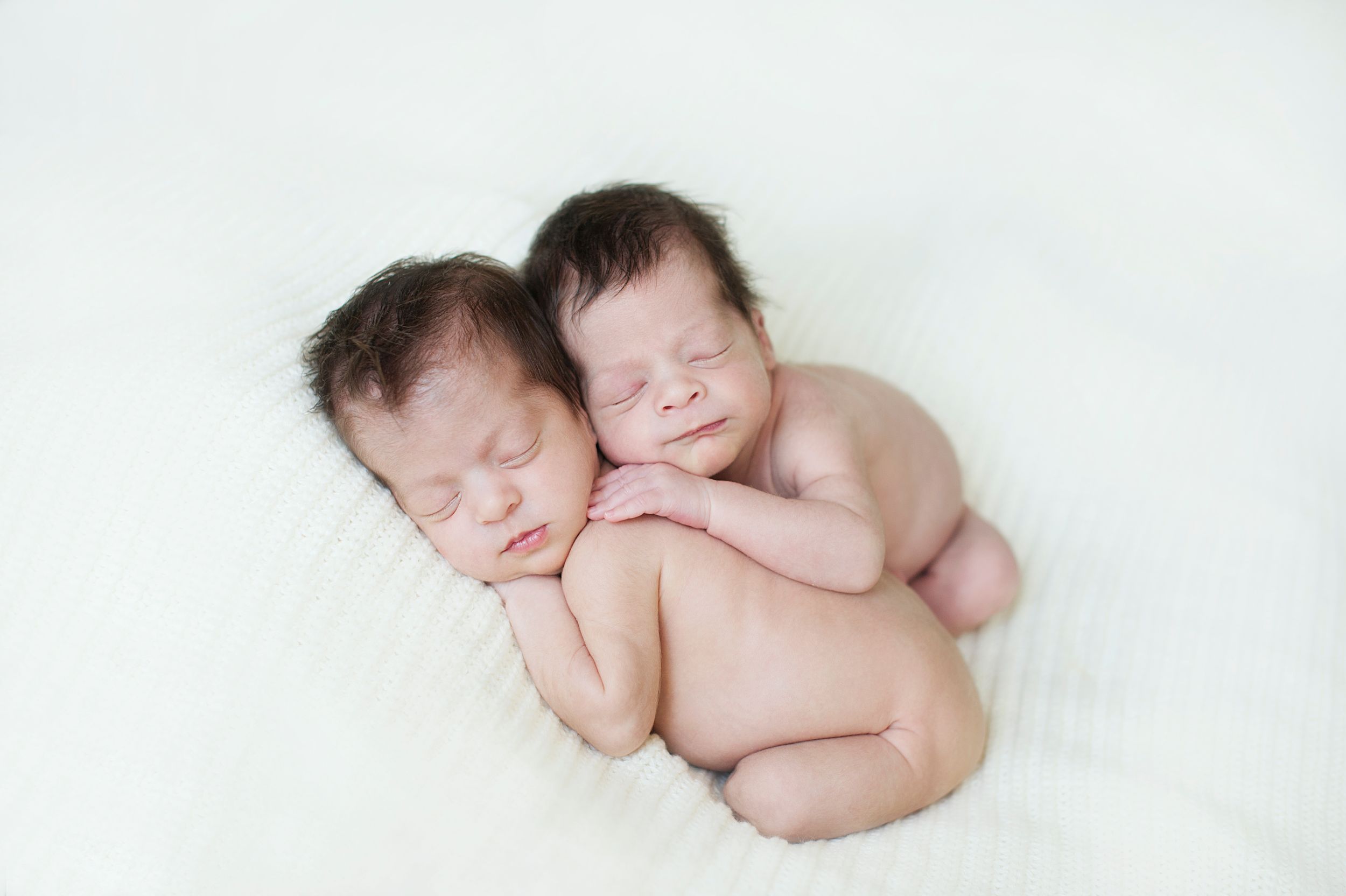 Newborn twins sleeping close together on a white blanket during a Toronto photo shoot by Phoebe Lee Photo