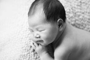 Newborn baby in a black-and-white portrait resting a tiny hand near their mouth, taken by Phoebe Lee Photo in Toronto