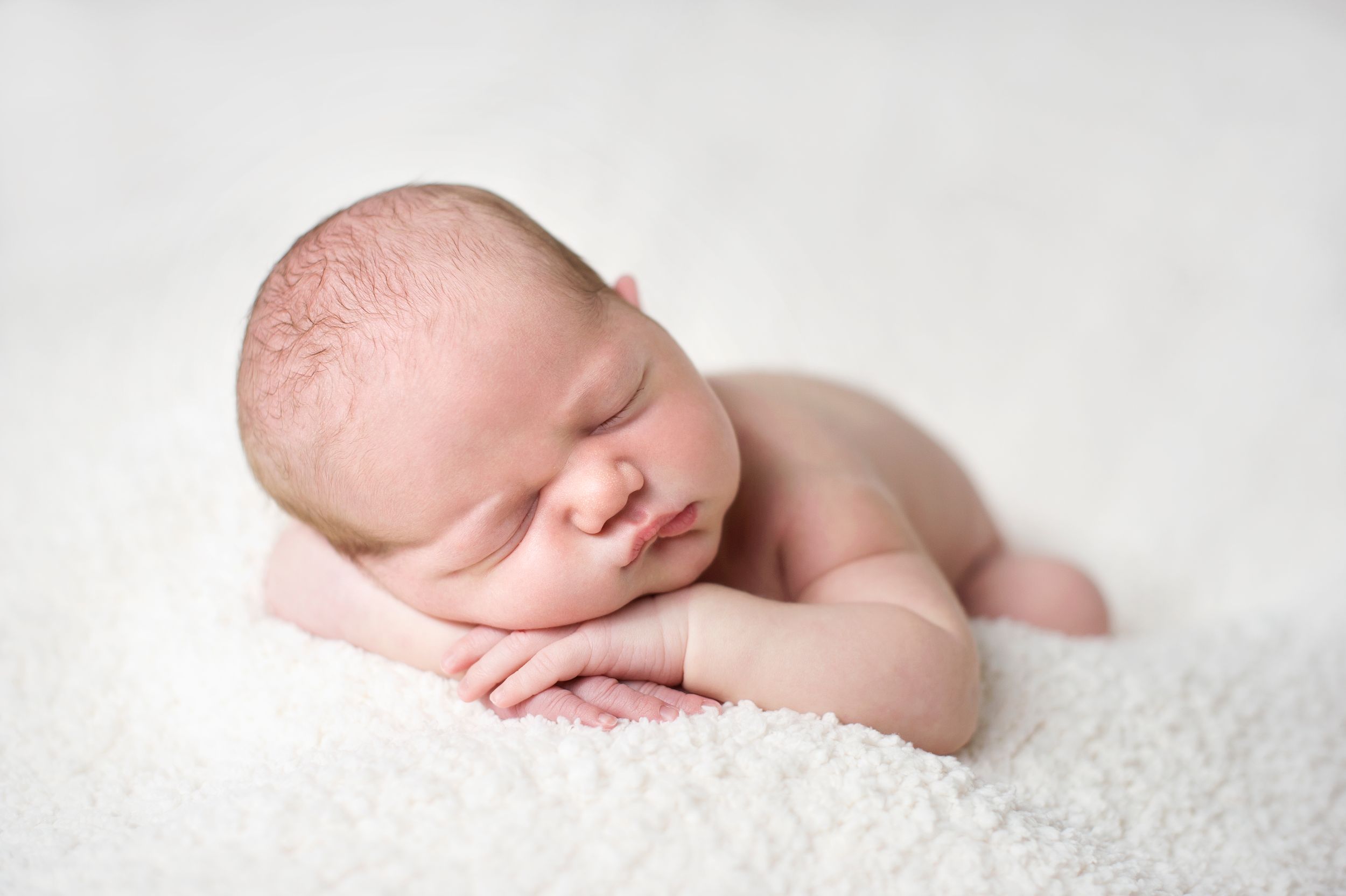 Newborn baby with chin on hands, dozing on a white blanket, captured by Phoebe Lee Photo in Toronto