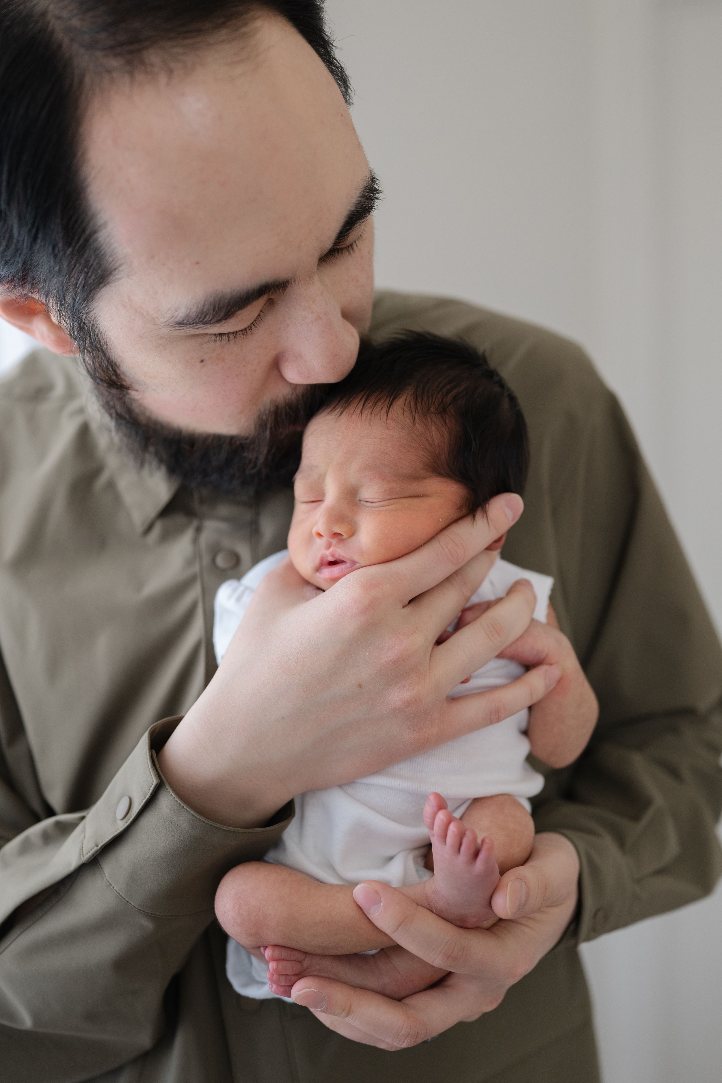 Father kissing newborn on head gently. Photographed by GTA newborn photographer Phoebe Lee Photo. Toronto baby photography.