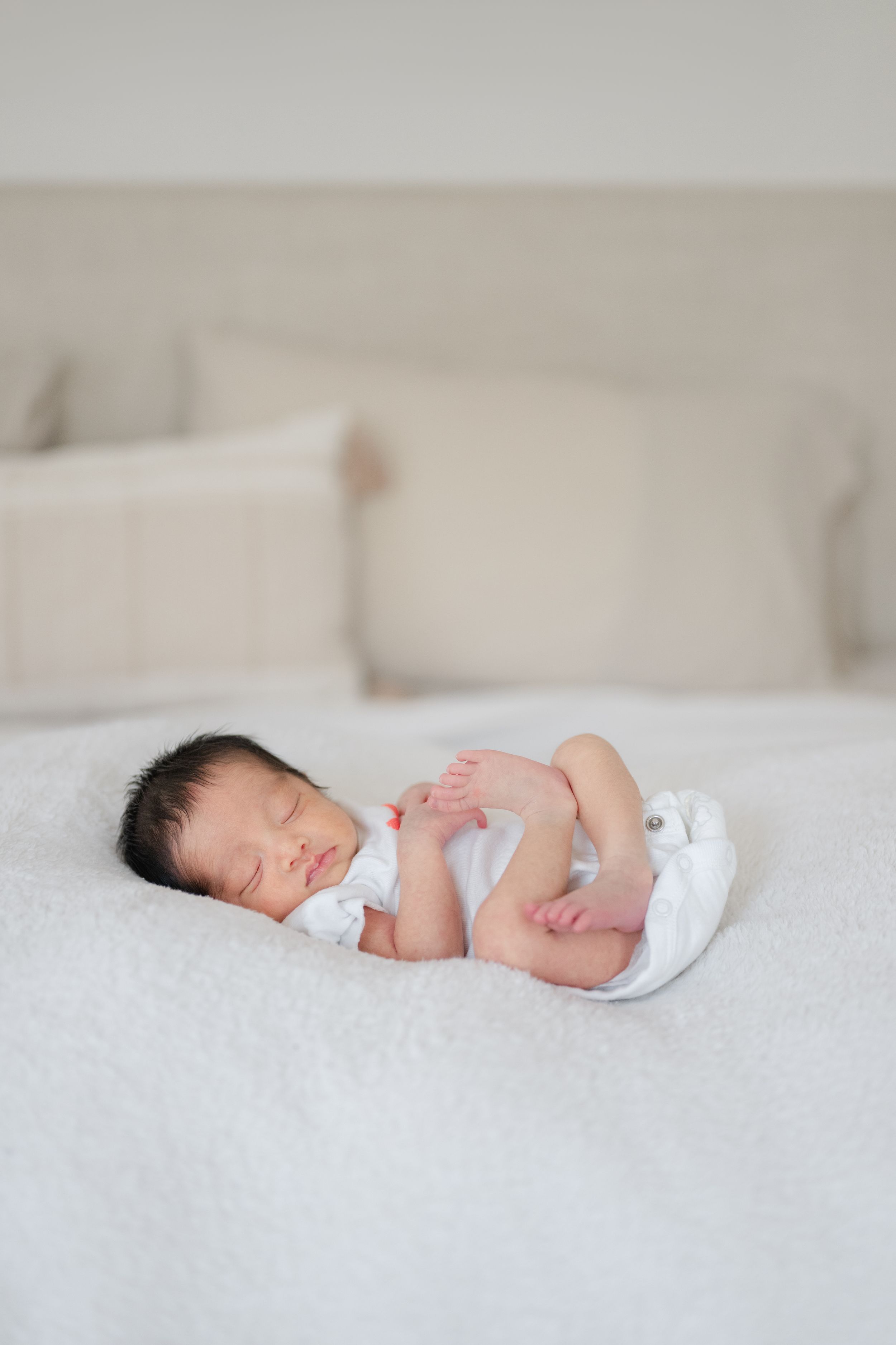 Sweet newborn baby sleeping peacefully on white bedding in soft natural light. Lifestyle photo shoot by newborn photographer Phoebe Lee GTA.