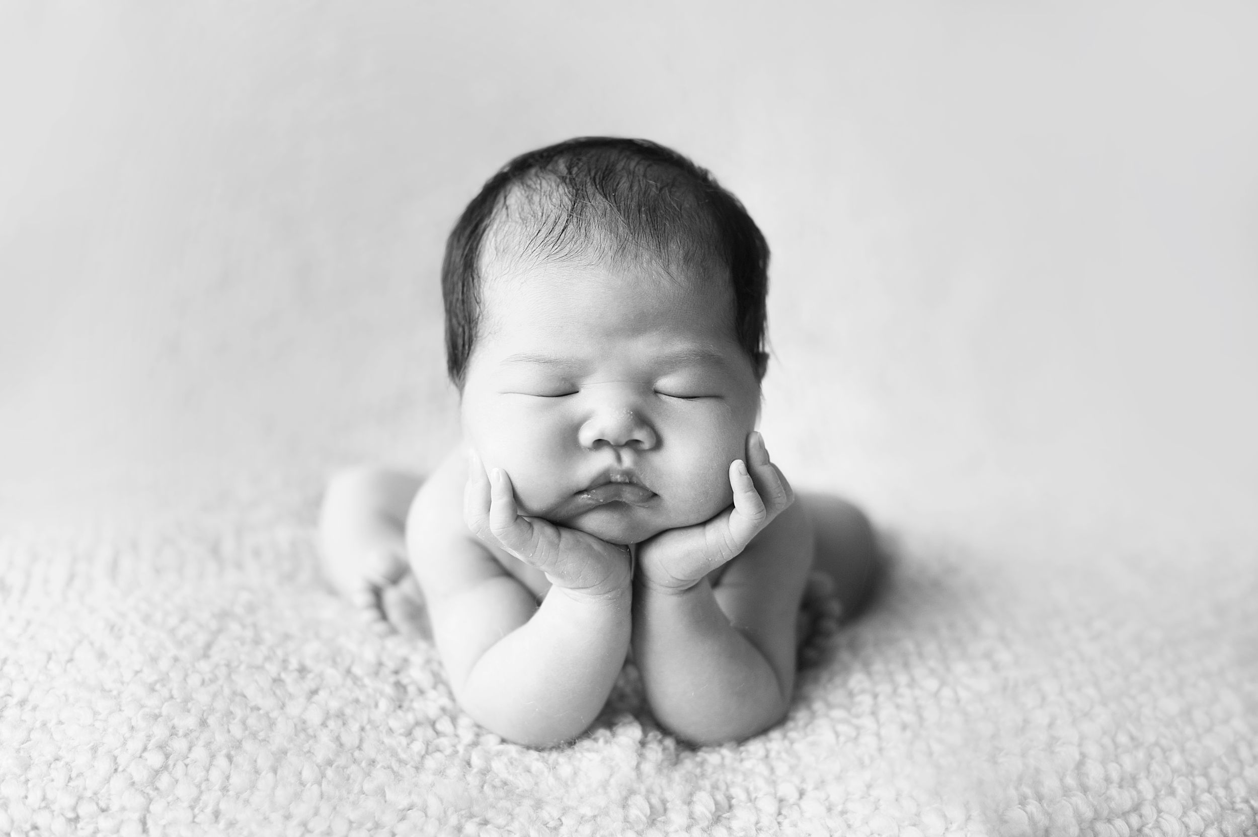 Black-and-white photo of newborn in the "froggy pose" on a textured blanket, captured by Phoebe Lee Photo in Toronto