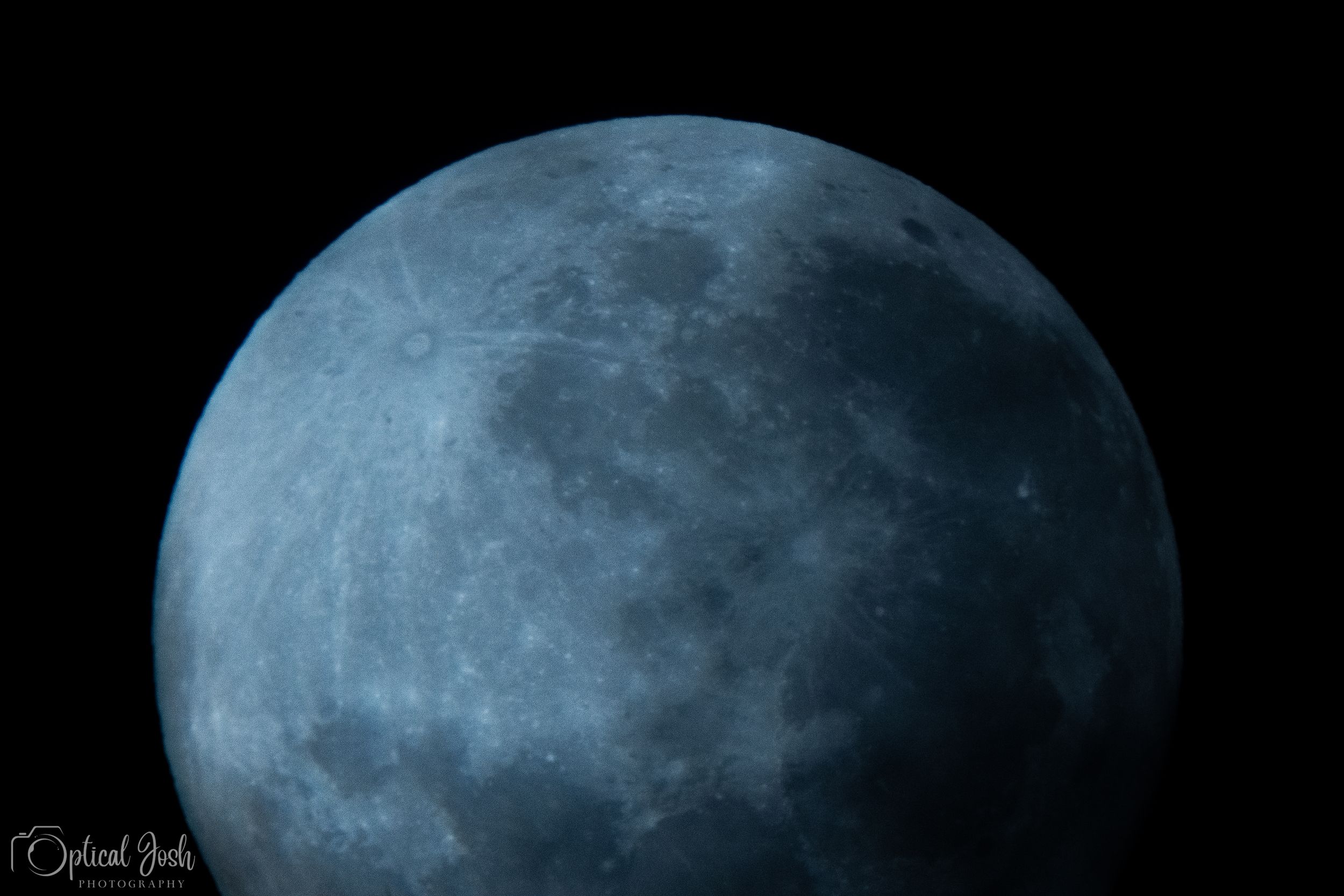 A close-up astronomical photo of the full moon in a bluish-tinted color against a dark night sky.