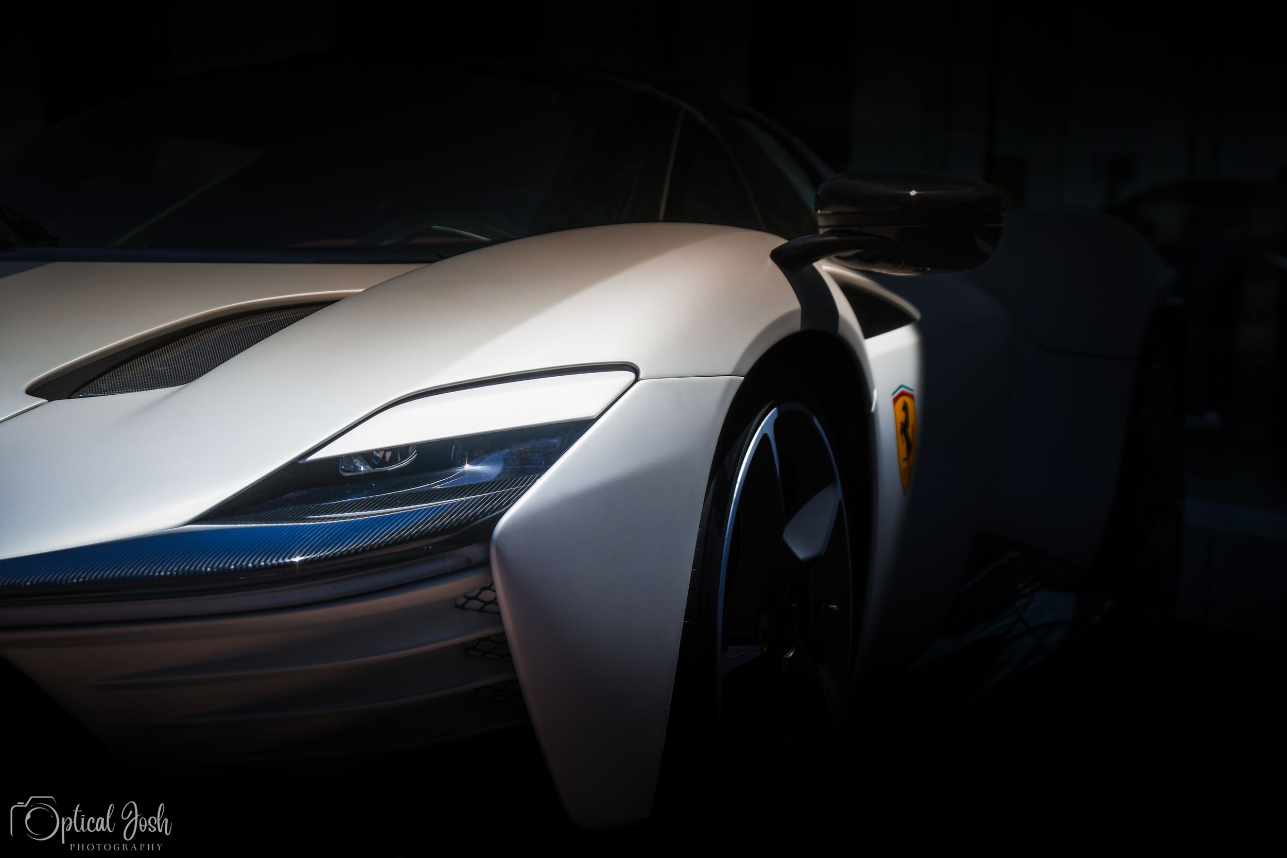 Close-up detail shot of a silver McLaren supercar's front headlight and wheel arch in dramatic lighting.