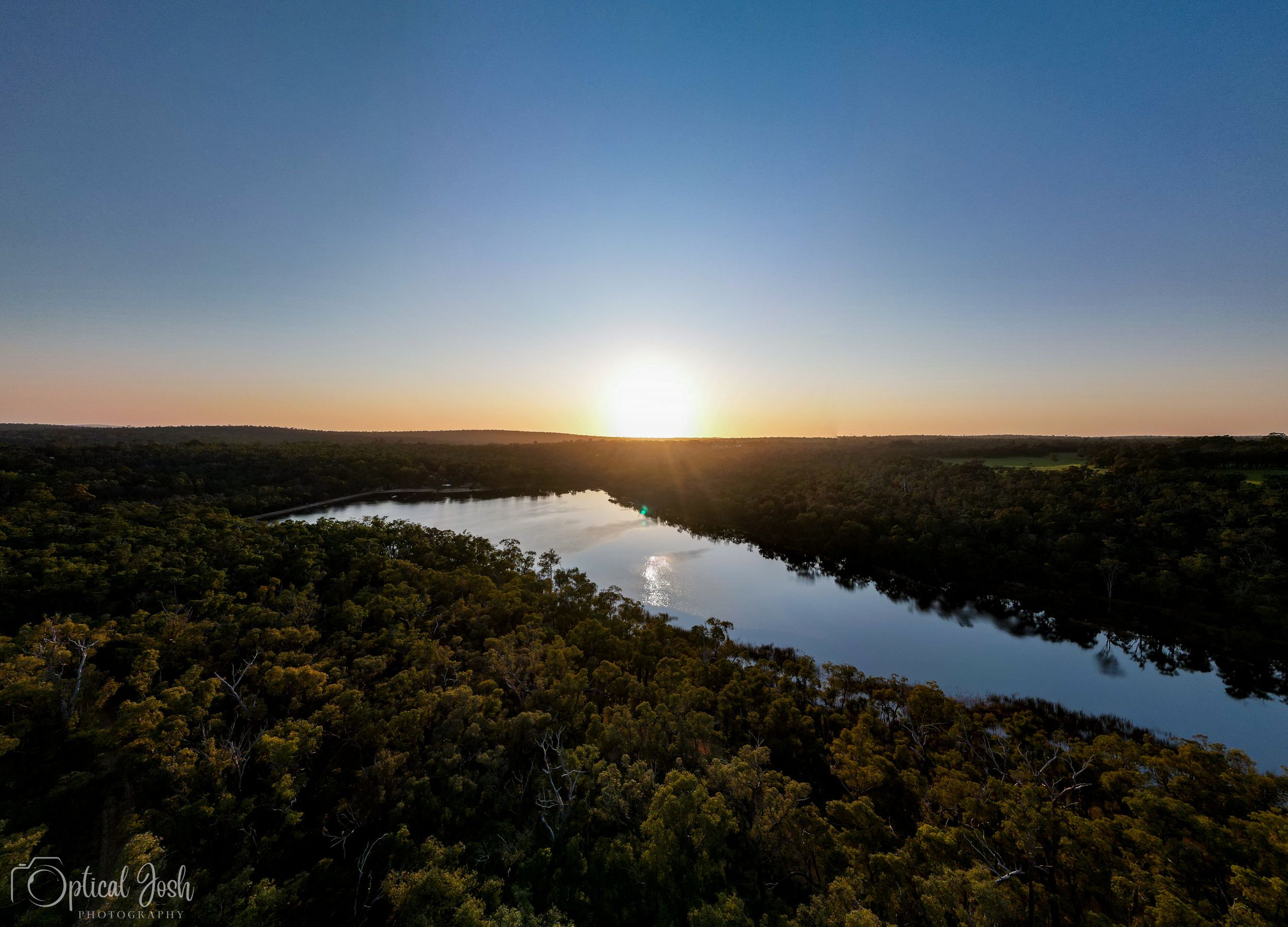 Aerial sunset view over winding river through lush green forest landscape with golden sunlight reflecting on calm waters.
