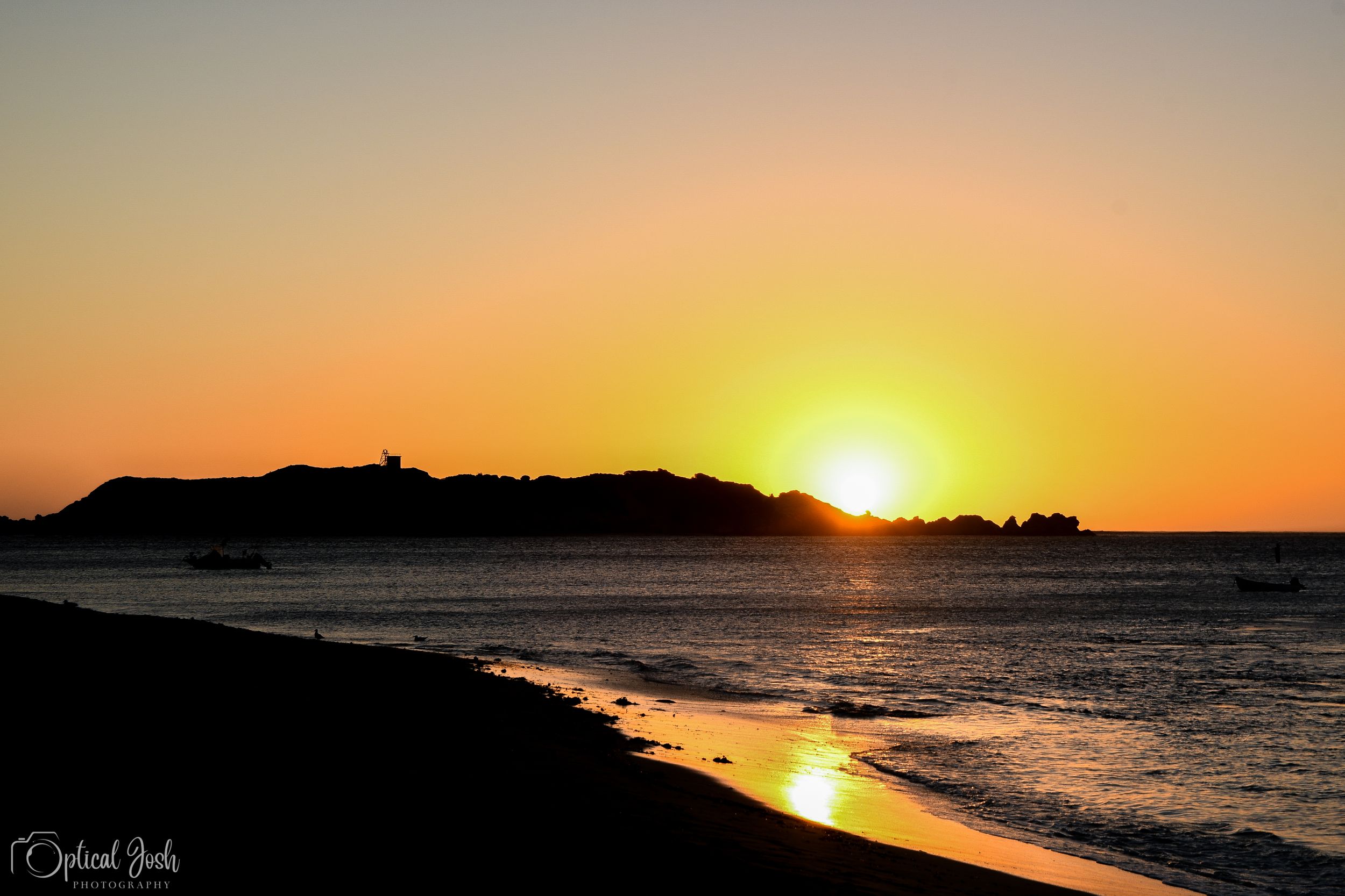 Golden sun setting over a coastal landscape with waves gently rolling onto a beach at dusk.