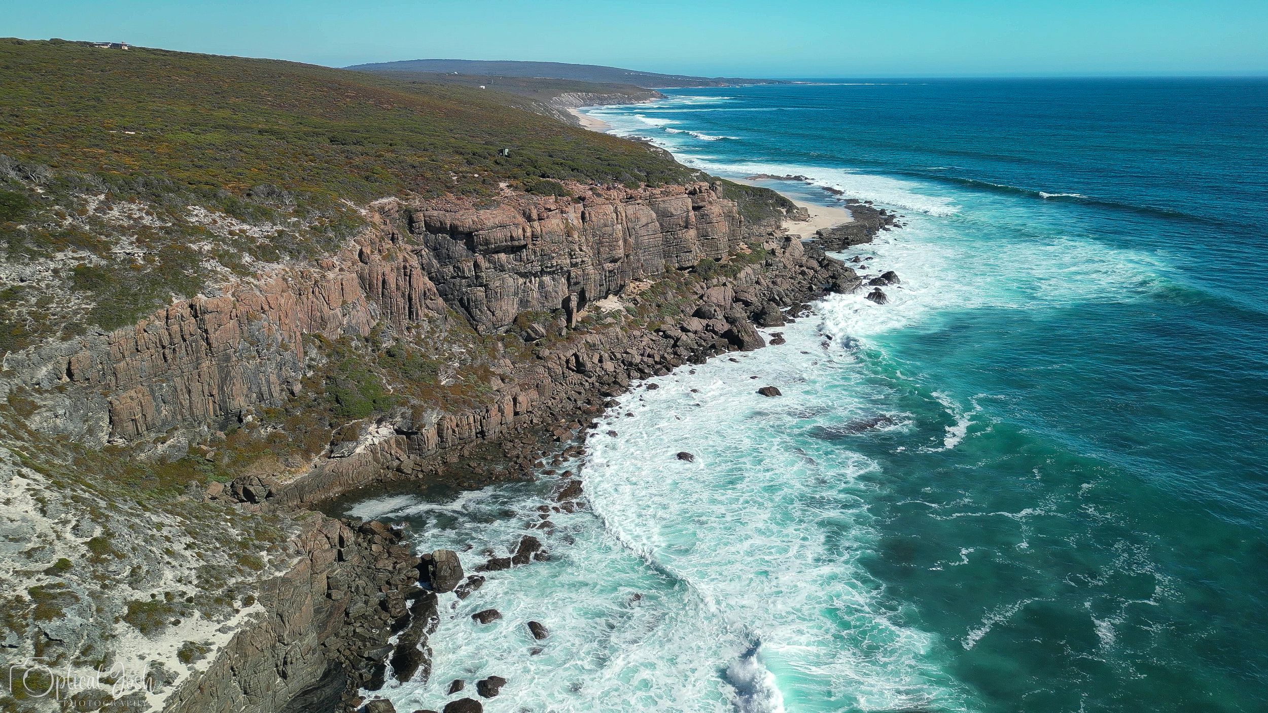 Aerial view of rugged coastal cliffs and turquoise waves crashing against rocky shoreline along a remote coastline.