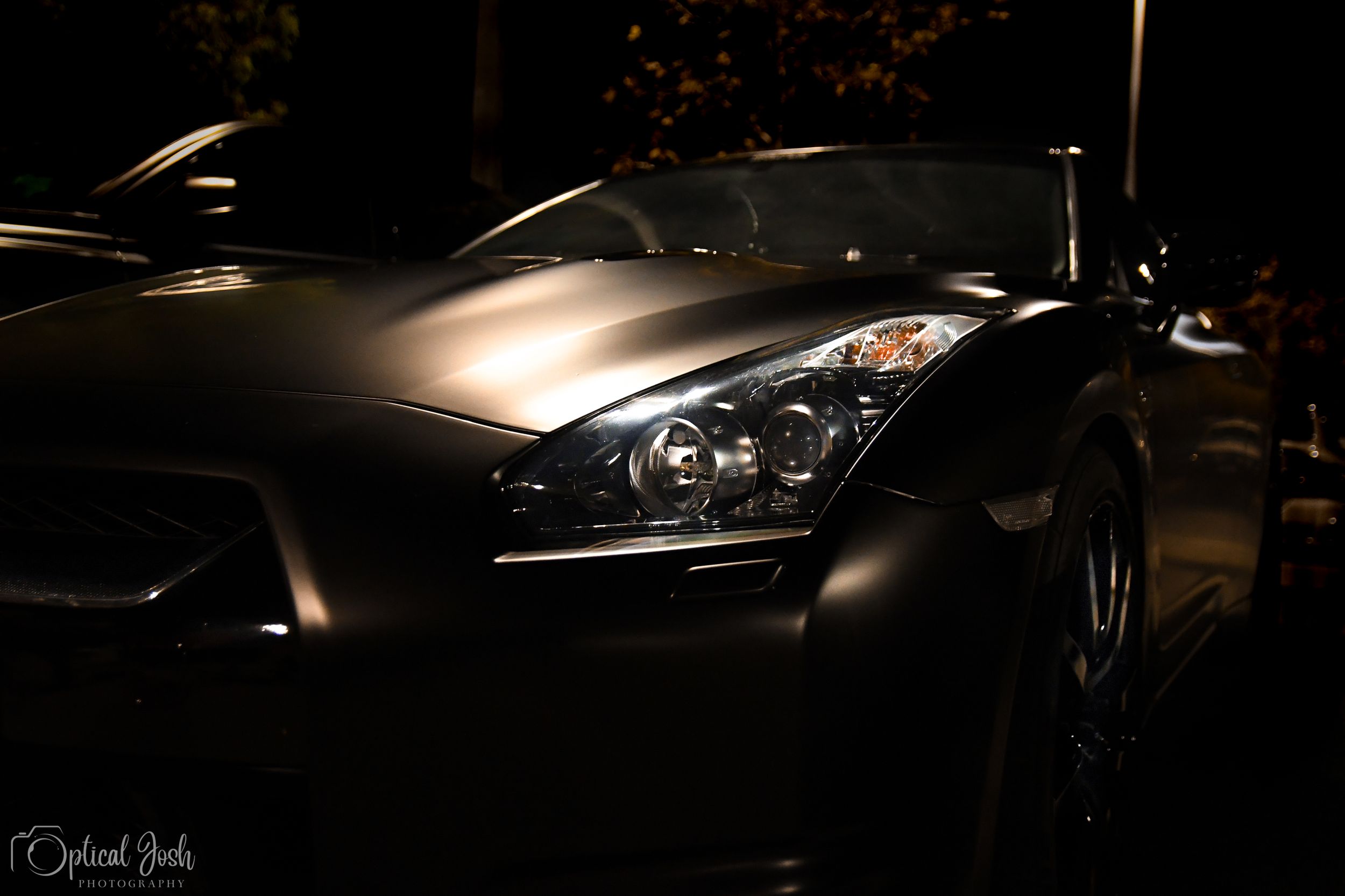 Sleek black sports car with distinctive headlights photographed in low light conditions showing front quarter view details.