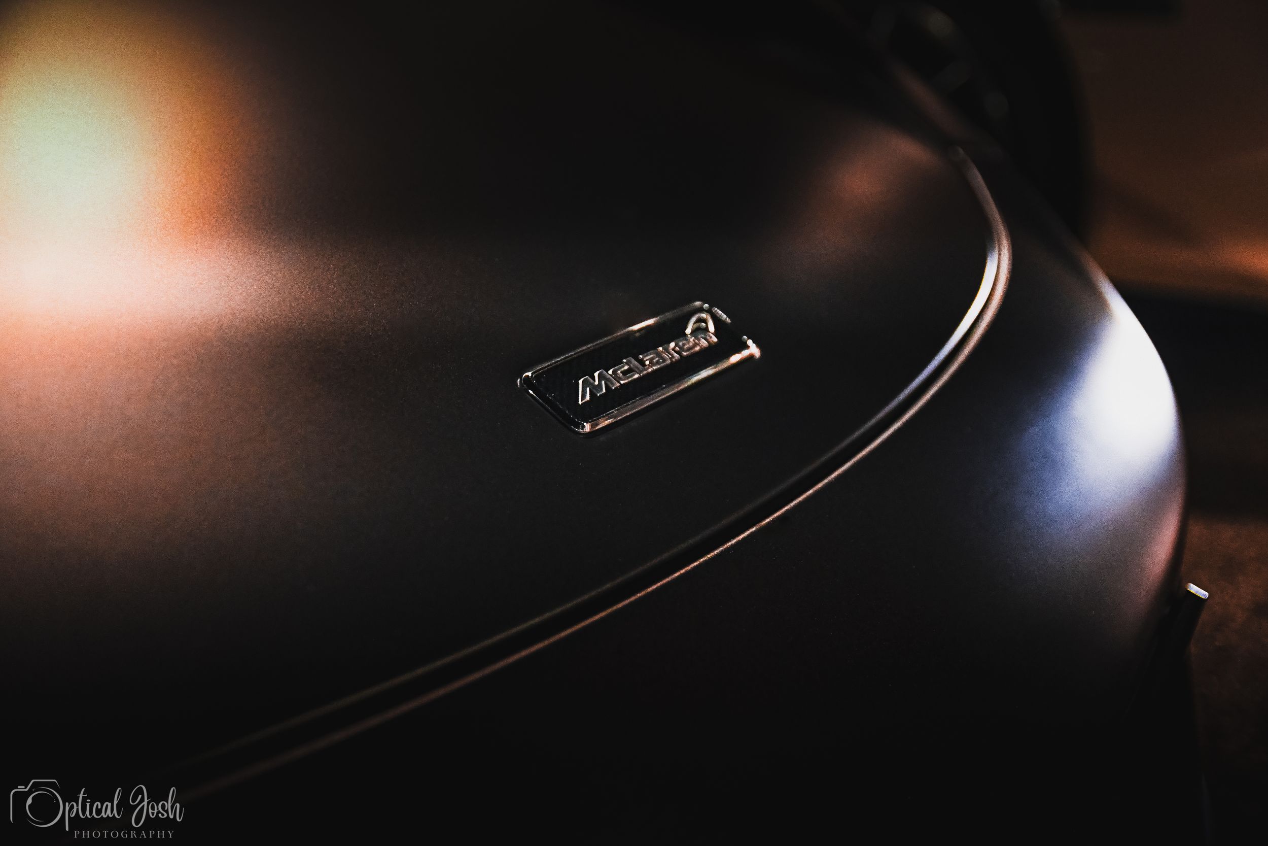 Close-up macro shot of a black curved surface with a metallic triangle logo detail in low light conditions.