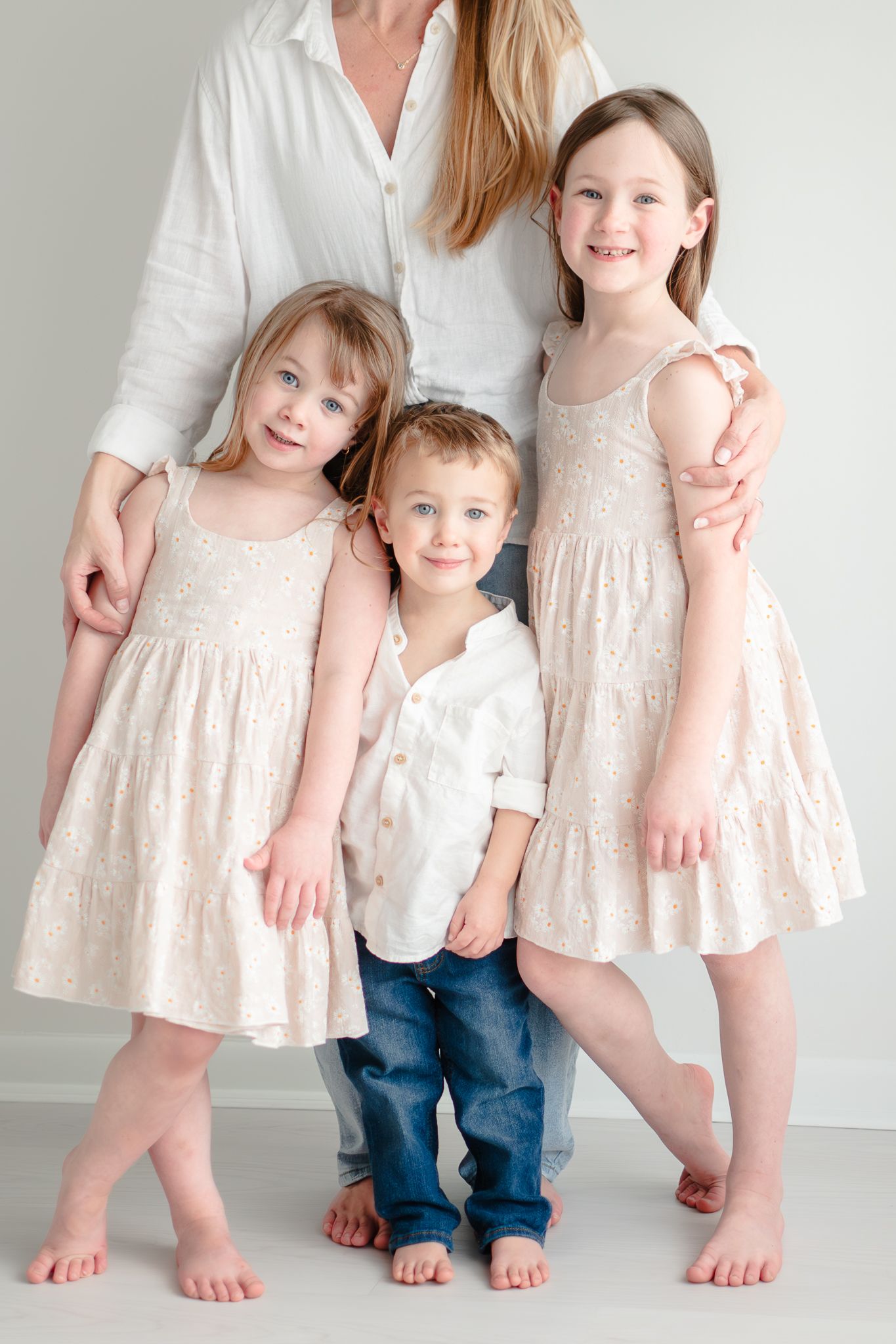 Light portrait of children and adult in coordinating cream and white outfits standing against white background.