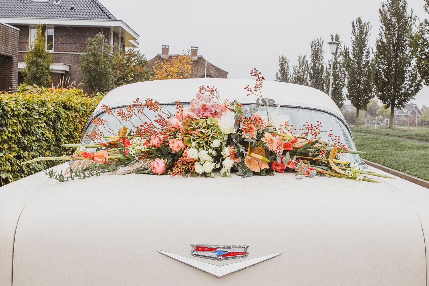 Vintage white car decorated with pink and peach floral arrangement on the trunk. Trouwauto vintage.
