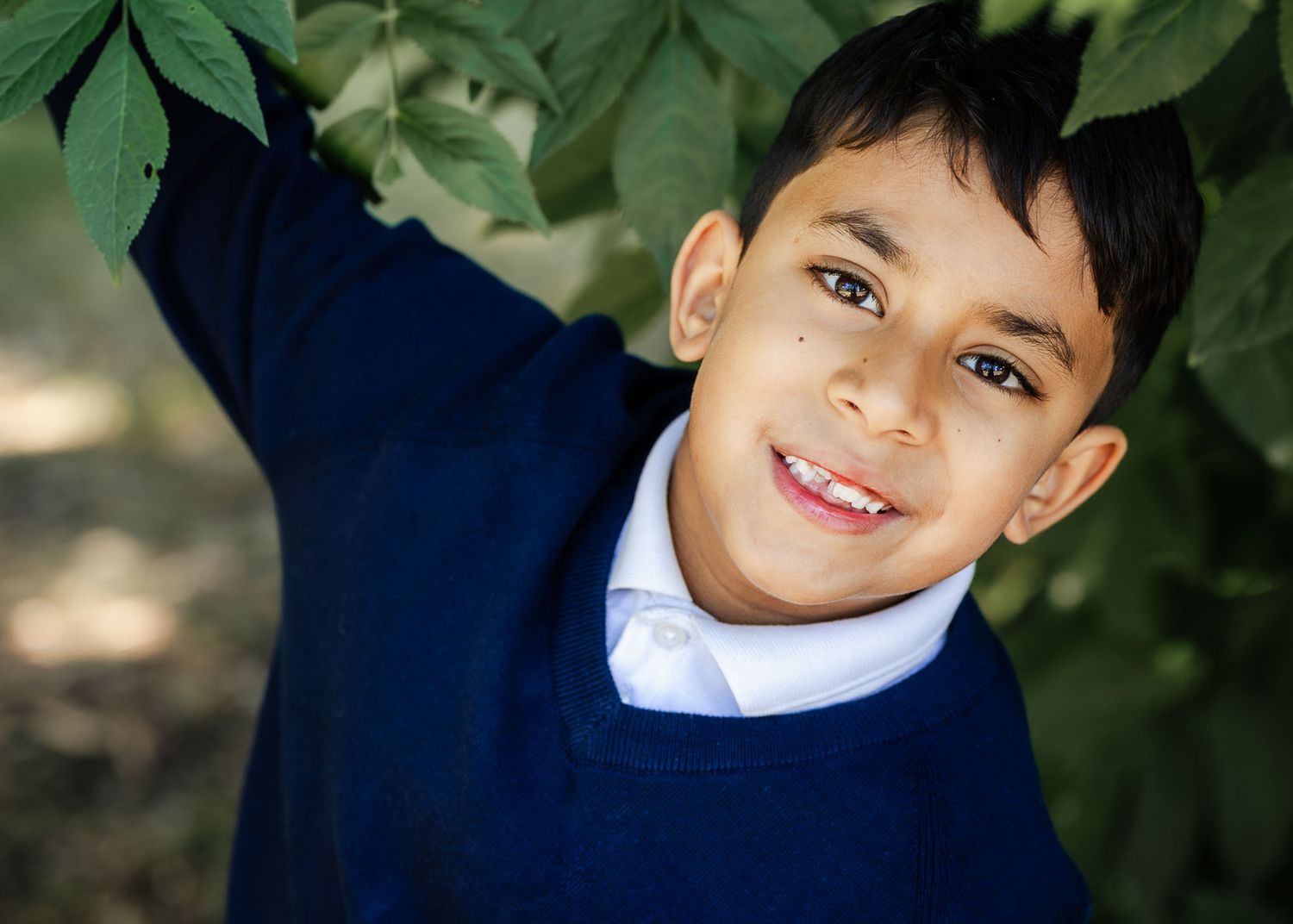 A school boy looks happy and relaxed as he sits under a tree having his school photograph taken. Bristol nursery and school photographer